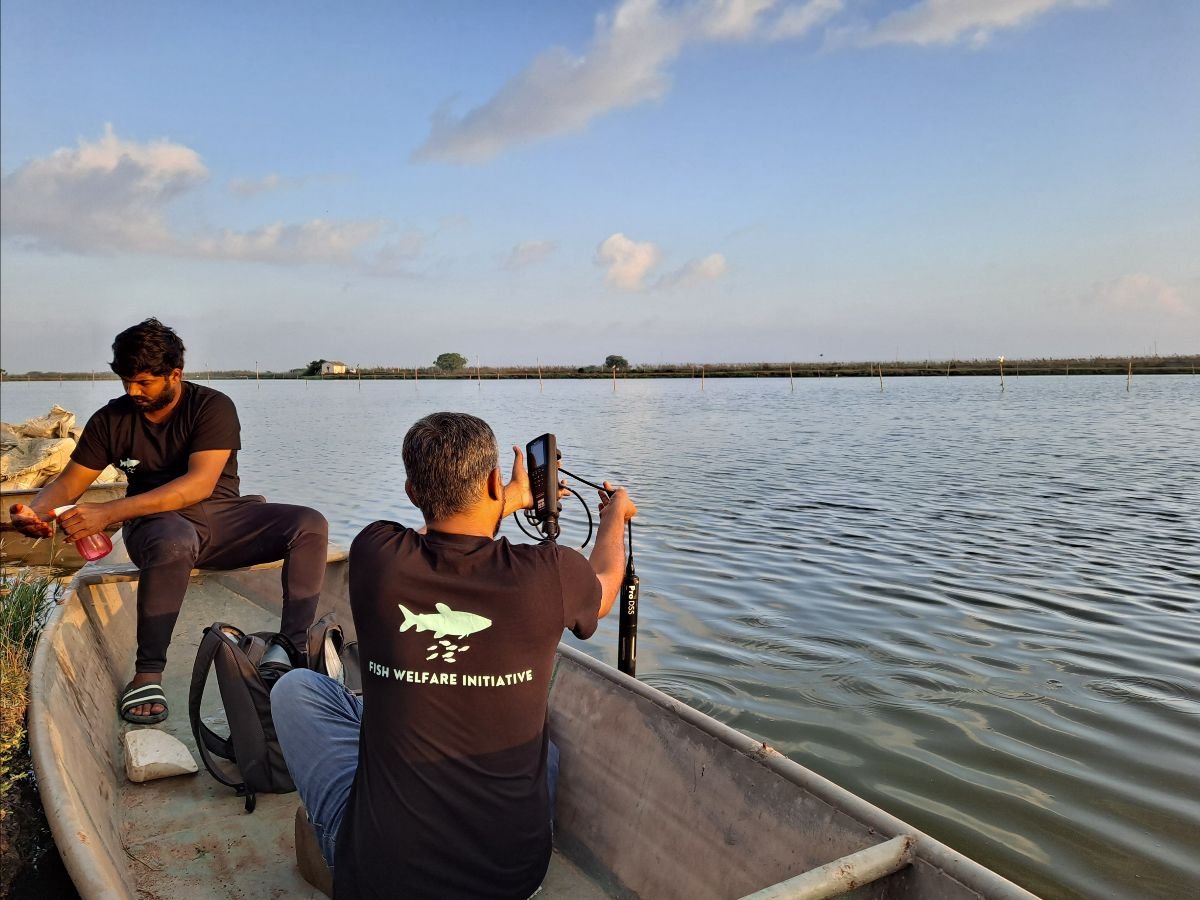 Two men fishing on a boat in a large body of water, with one man holding a fishing rod and the other man sitting nearby, in an outdoor setting with a partly cloudy sky.