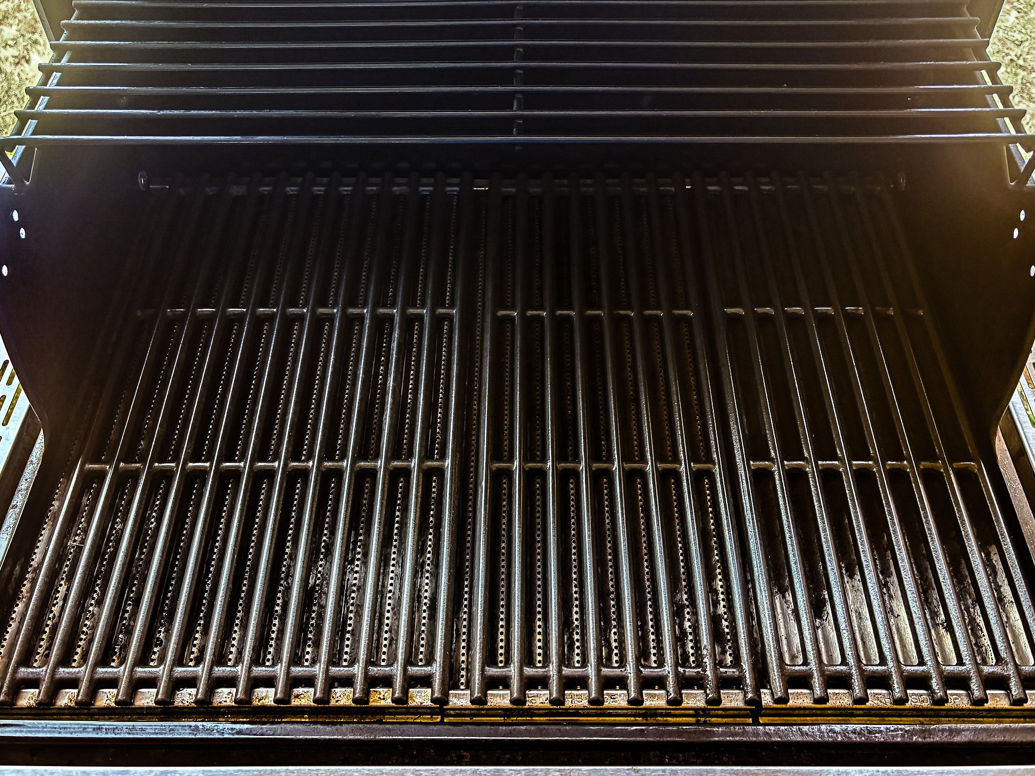 Close-up of a black metal grill with parallel bars, possibly a barbecue or grill grate, with some signs of rust and dirt.