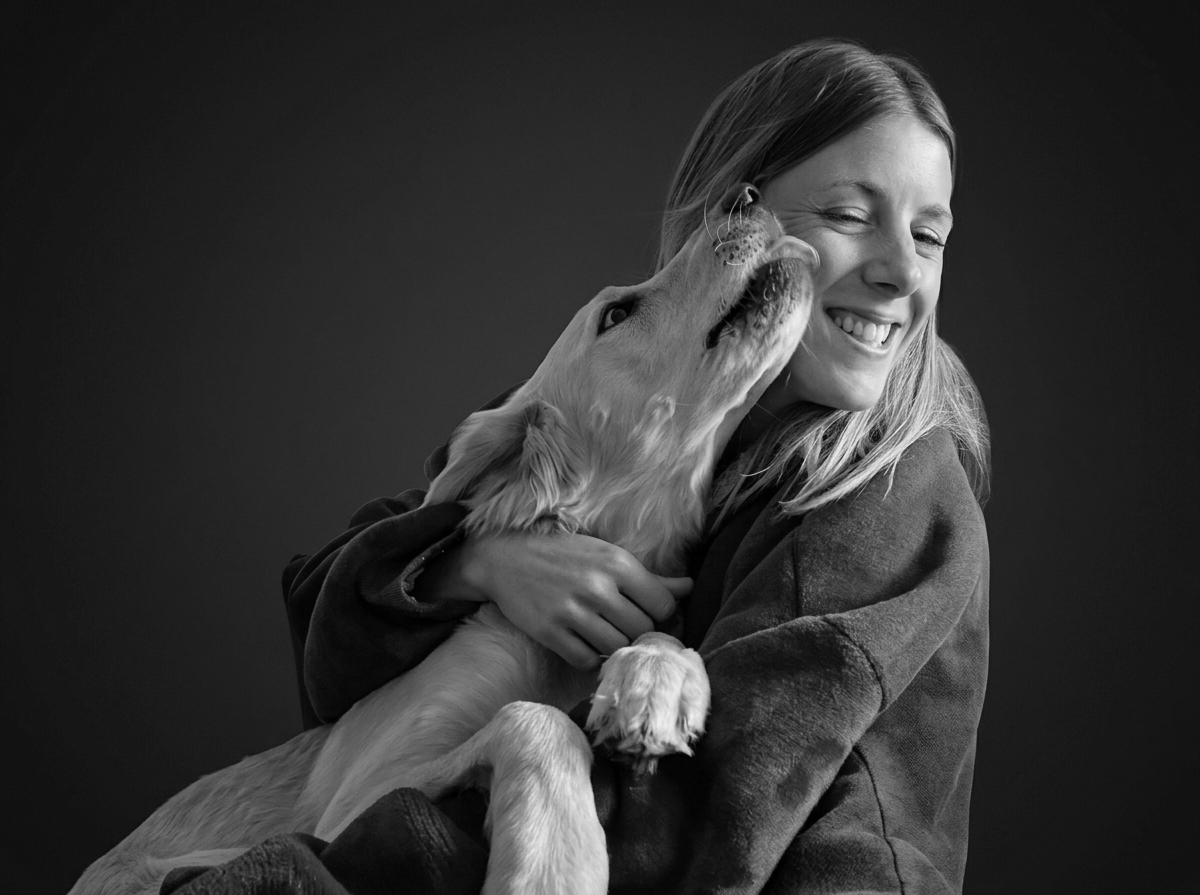 Une femme souriante embrassant un chien blanc dans une photo en noir et blanc.