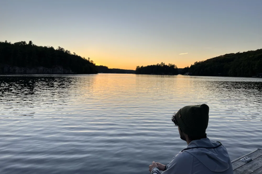 Person wearing a dark knit beanie looking across a lake at sunset