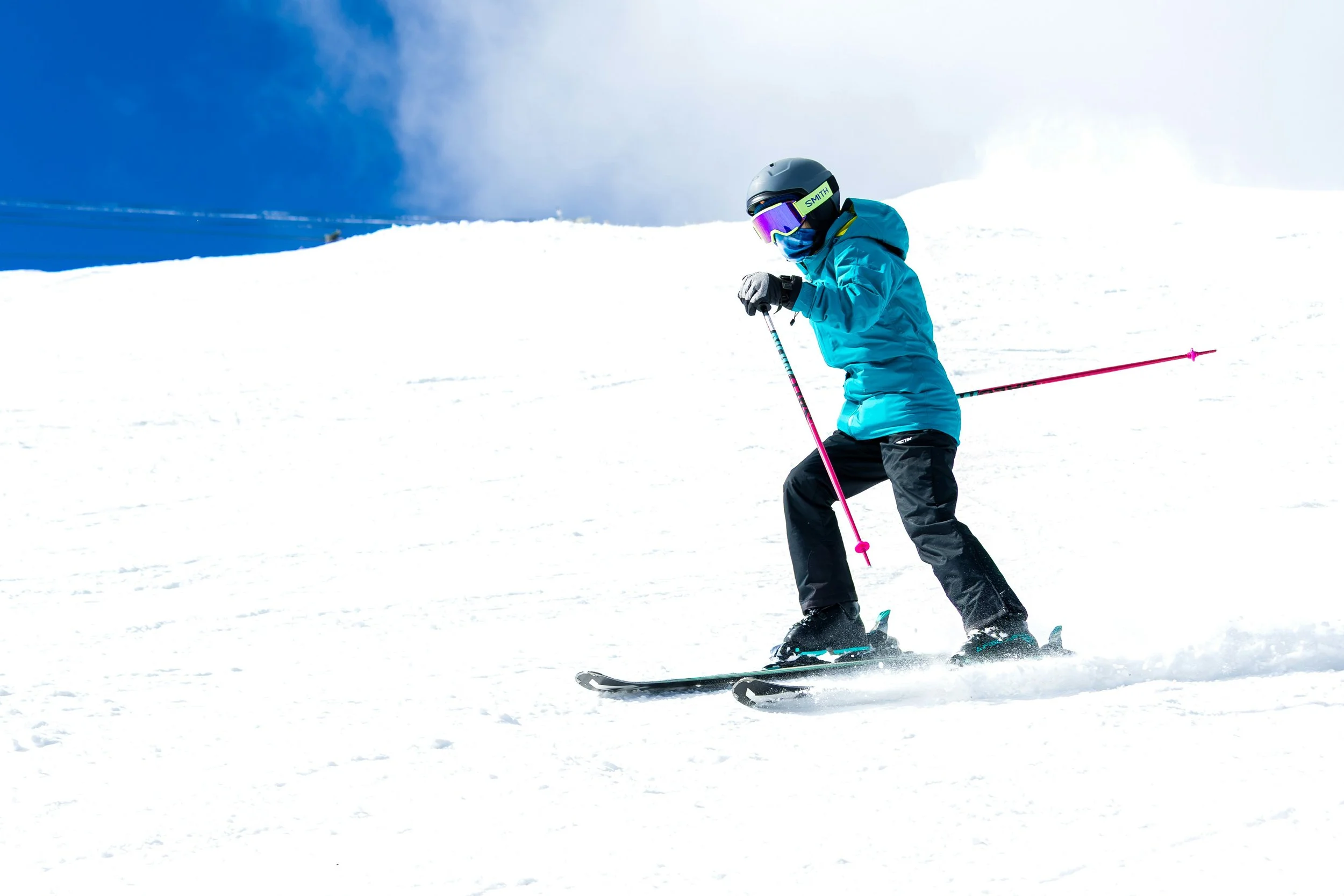 Skier in a blue jacket skiing down a snowy mountain