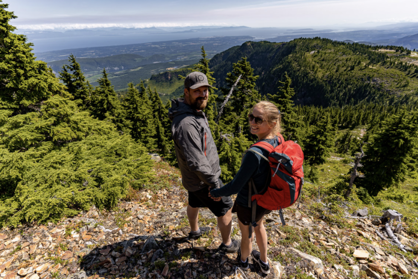 Two hikers standing on a mountain trail overlooking a forested valley