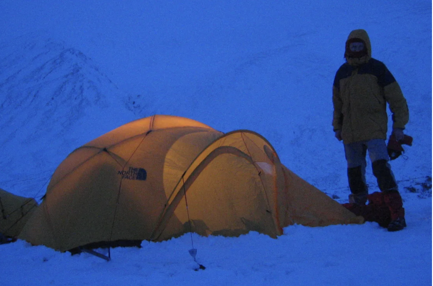 Orange camping tents pitched in deep snow at dusk