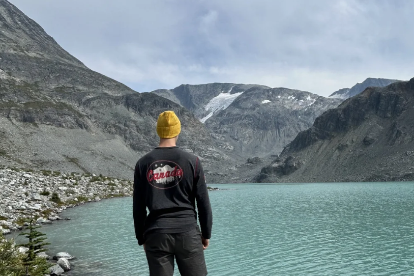 Person wearing a yellow knit beanie overlooking a turquoise alpine lake and mountains