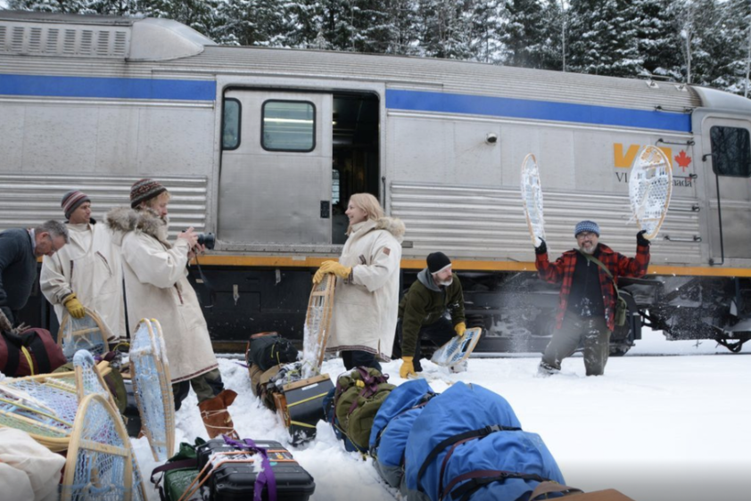 Group of people organizing outdoor gear beside a trailer in snowy winter conditions