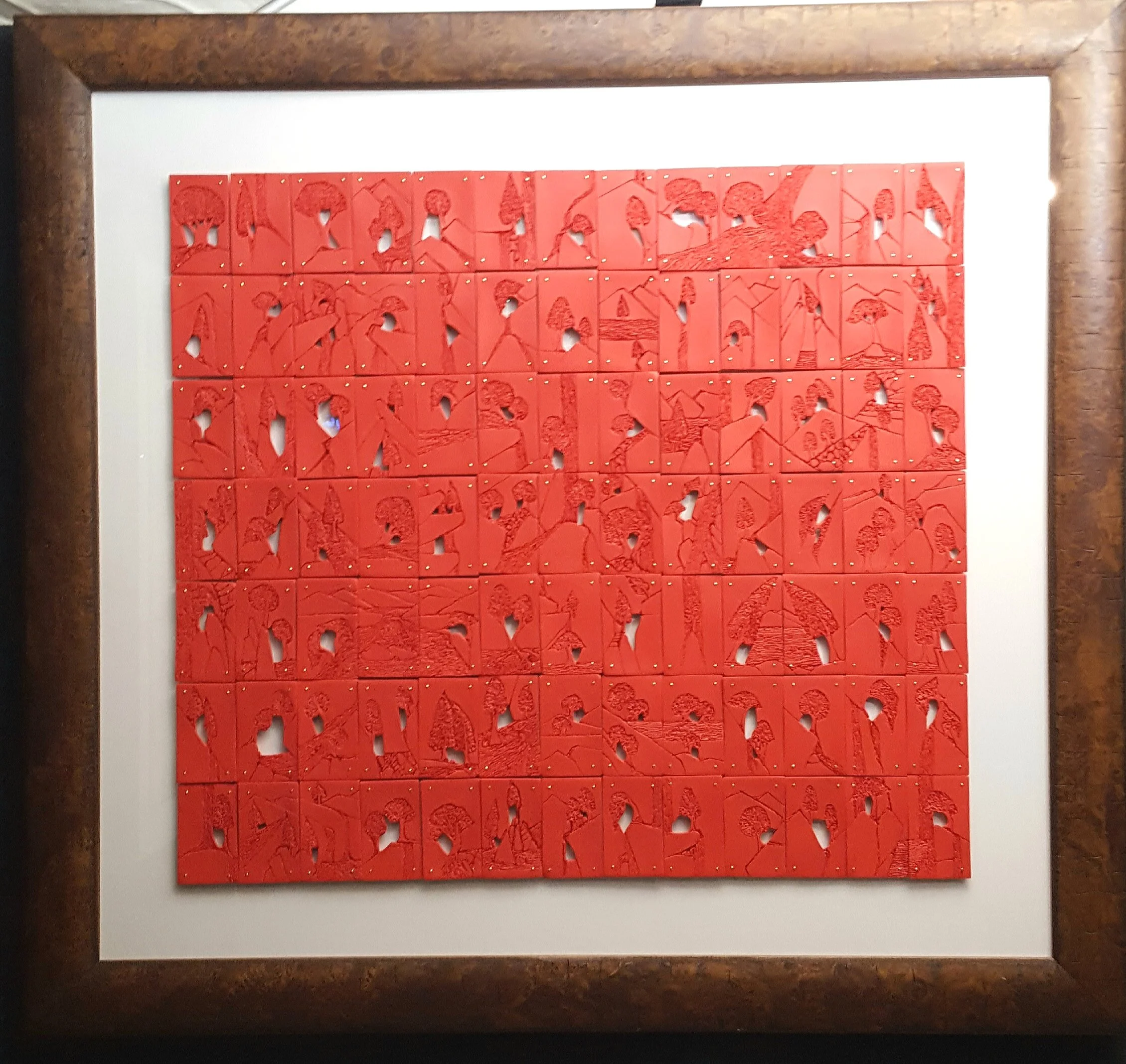Framed artwork composed of small, red, engraved panels arranged in a grid, featuring nature and rural scene outlines in a minimalist style.