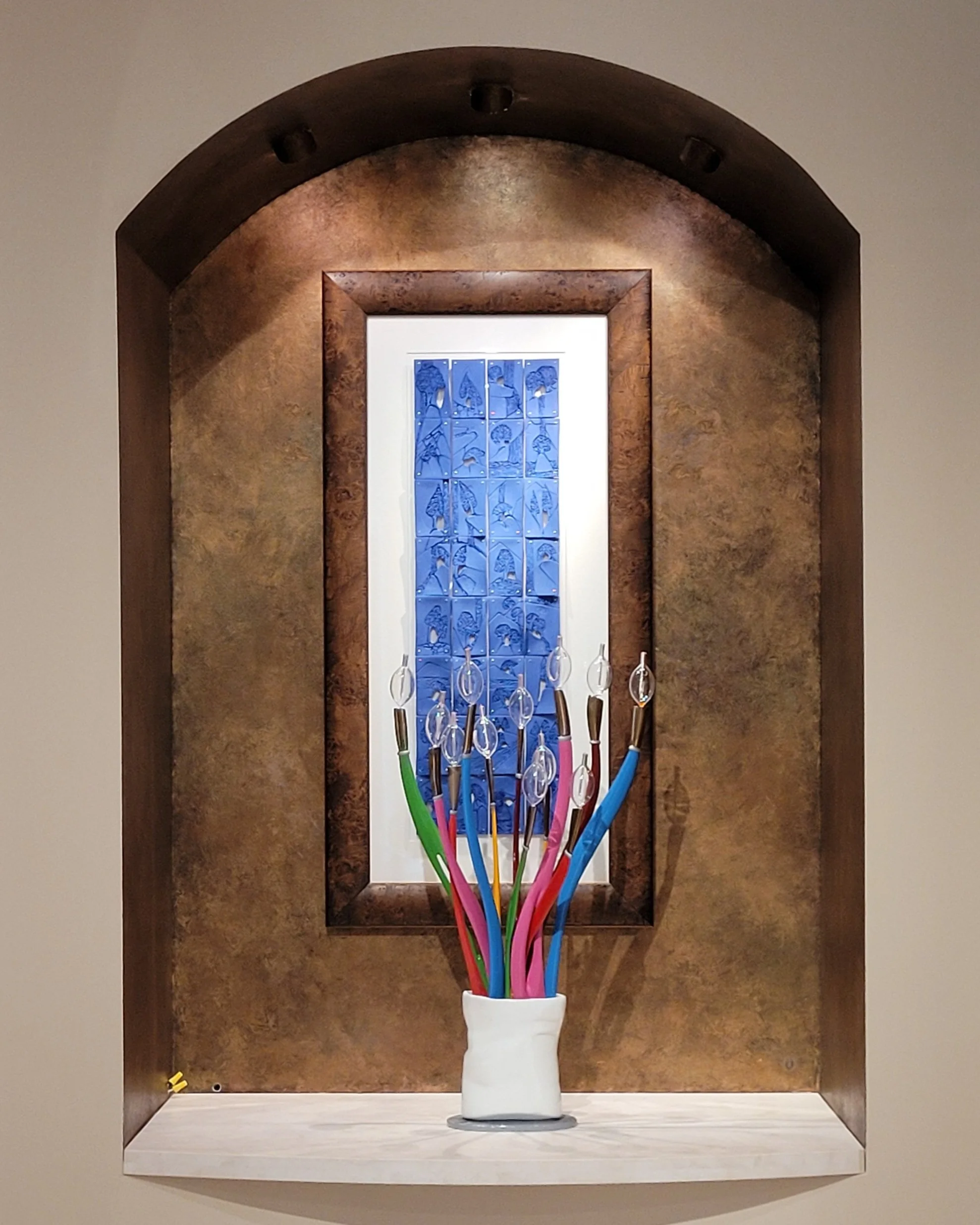 A set of 32 blue porcelain tiles in a walnut burl frame displayed inside an arched niche with a brown marble-like interior.