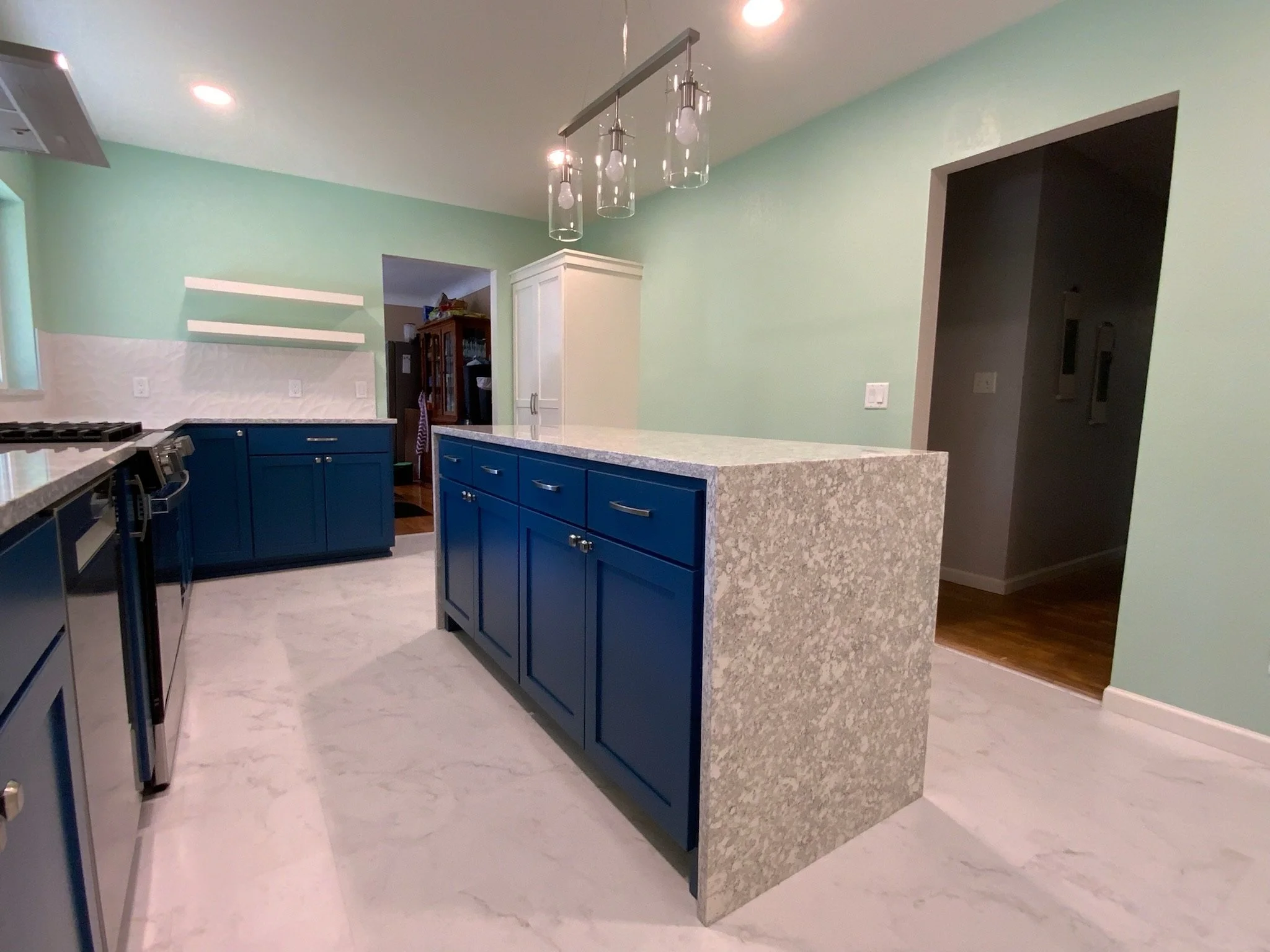 Modern kitchen with blue cabinets, granite countertops, green painted walls, and pendant lighting.