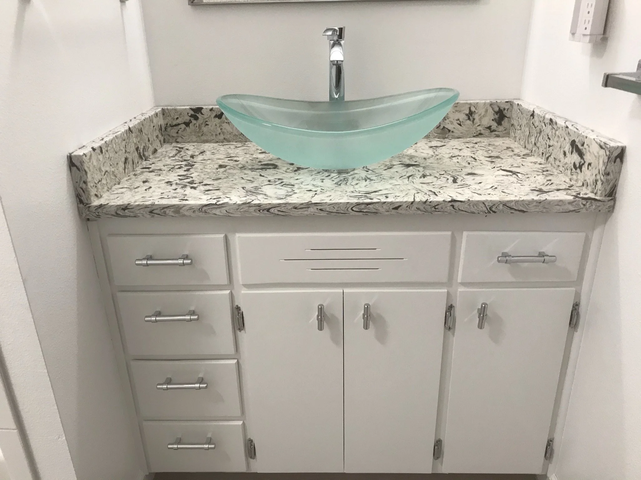A bathroom vanity with a granite countertop, white cabinets, and a glass vessel sink with a modern chrome faucet.
