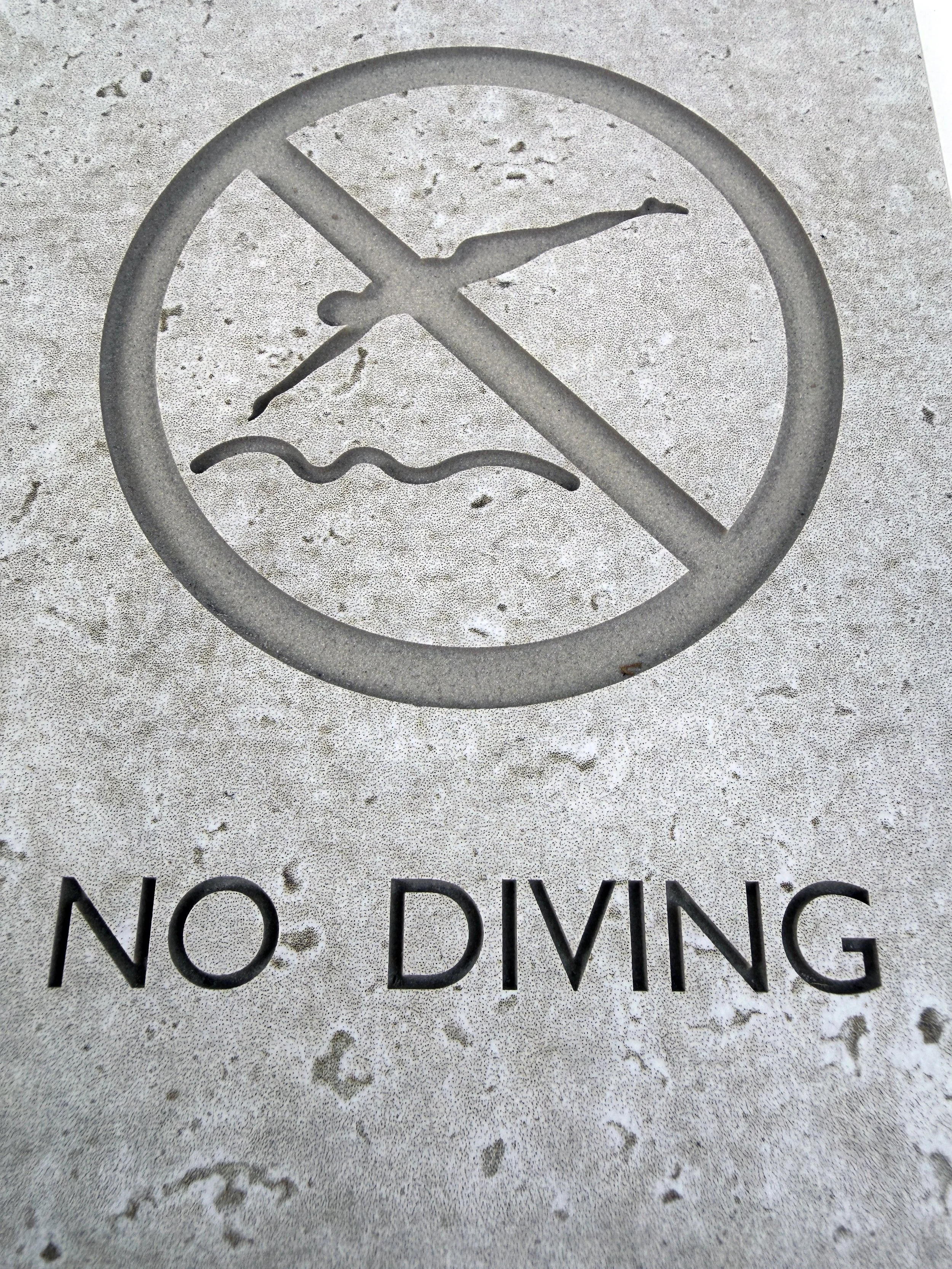 A painted sign on concrete with a symbol of a person diving and a line through it, indicating no diving.