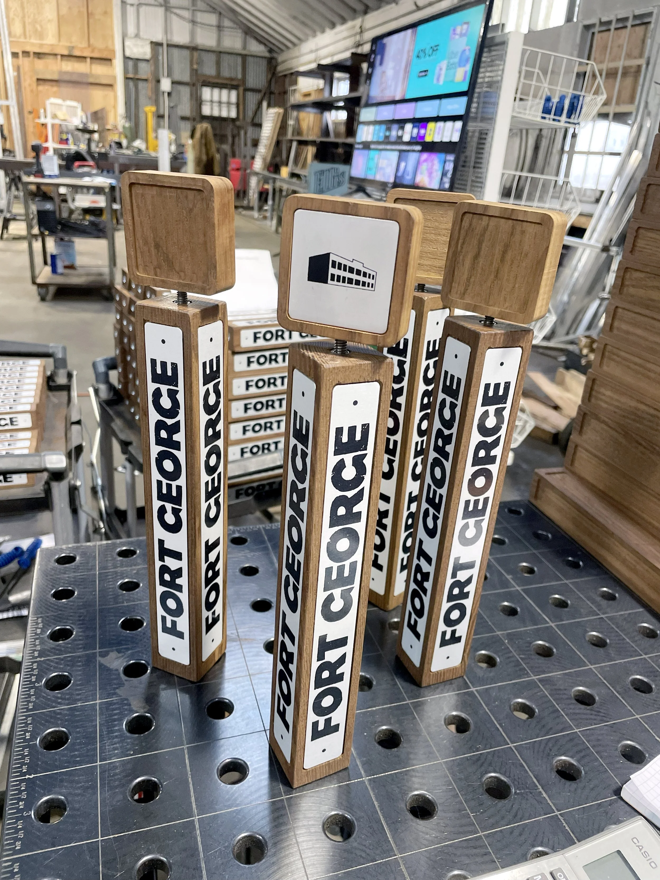 Wooden yard signs with 'FORCE' printed vertically on white backgrounds, standing on a workbench in a workshop.