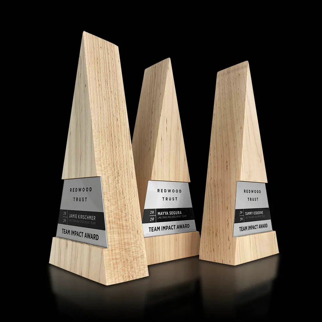 Three wooden team impact awards with engraved metal plaques, each with different recipient names, placed on a black surface against a black background.