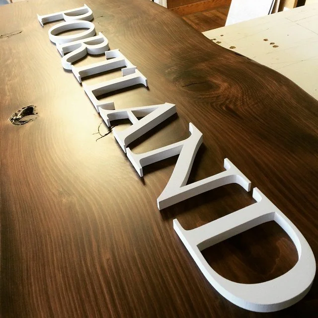 CO2 laser cut white 3D letters spelling 'DREAM' on a wooden table, custom laser cutting by MC Laser Labs.