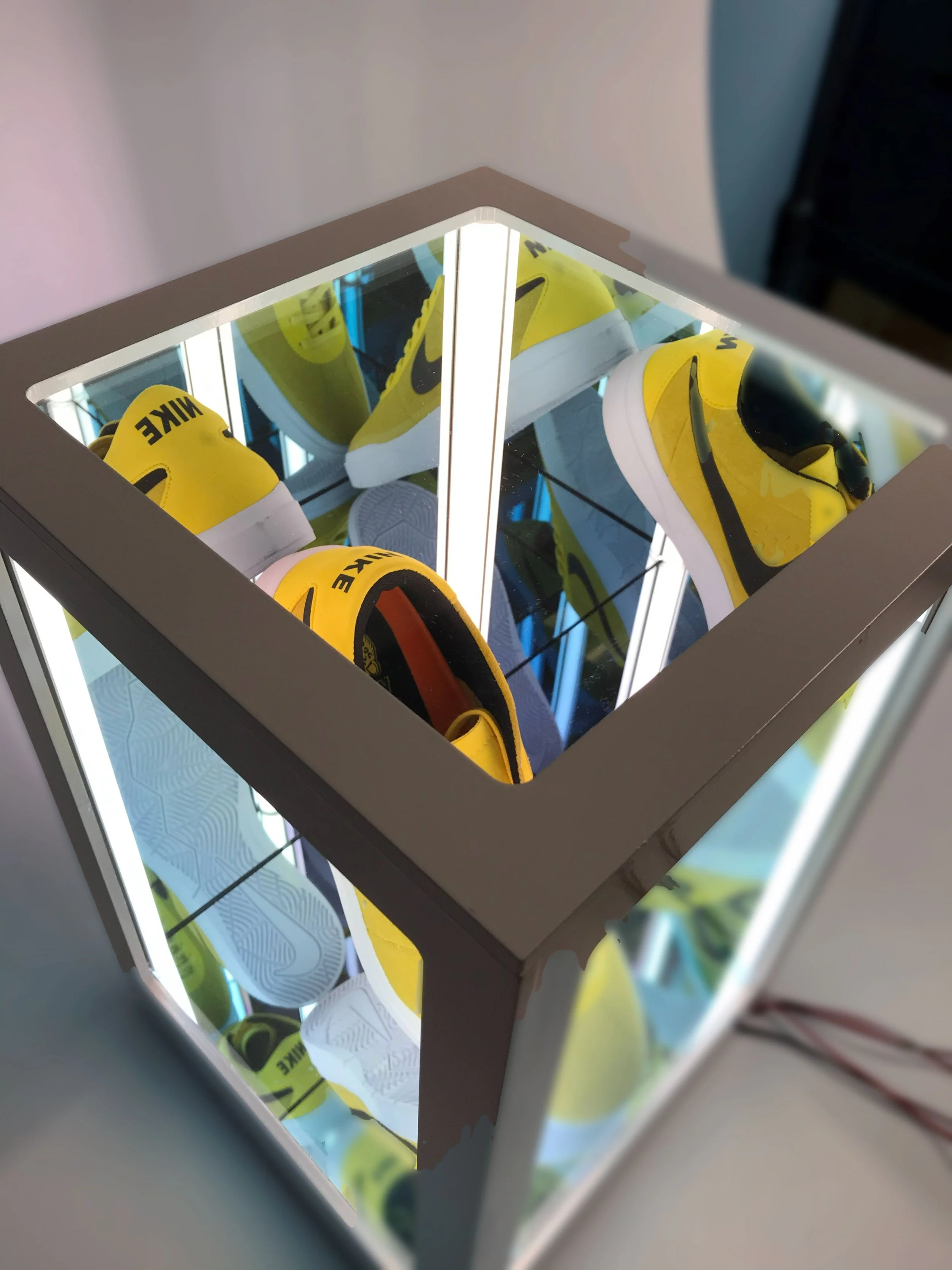 Yellow Nike sneakers a glass infinity box display, viewed from above. Custom fabrication and LED lighting by MC Laser labs 