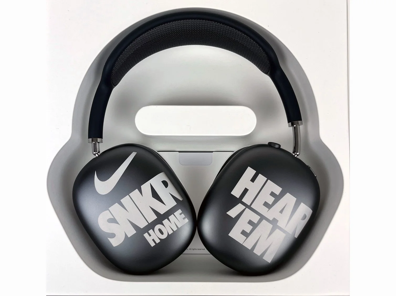 Black AIRPOD PRO headphones with the Nike logo laser engraved and the words 'HOME SWEAT HEAT' printed on the ears, placed inside a white carrying case.