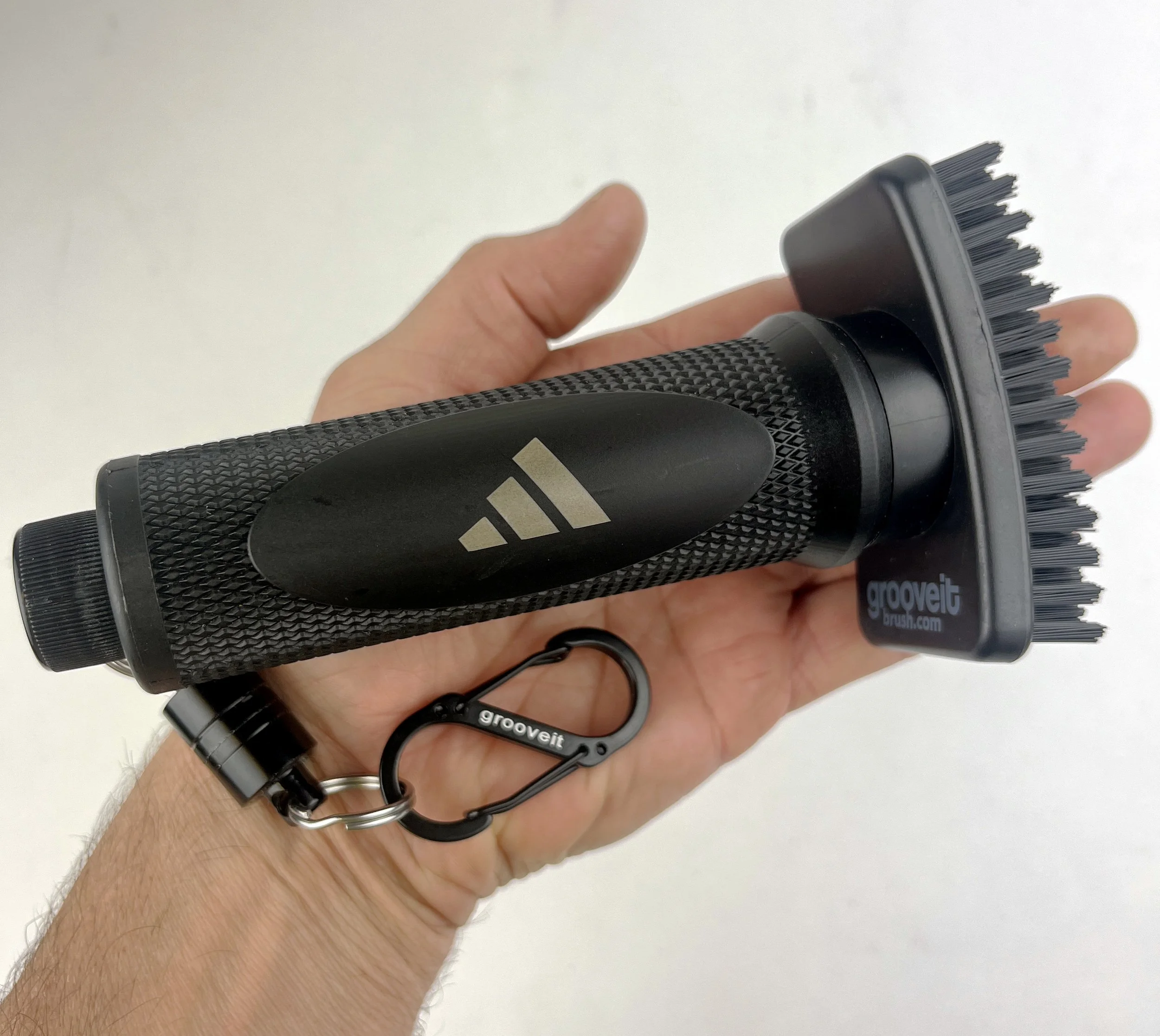 A person's hand holding a black grooming brush with a looped strap attached.