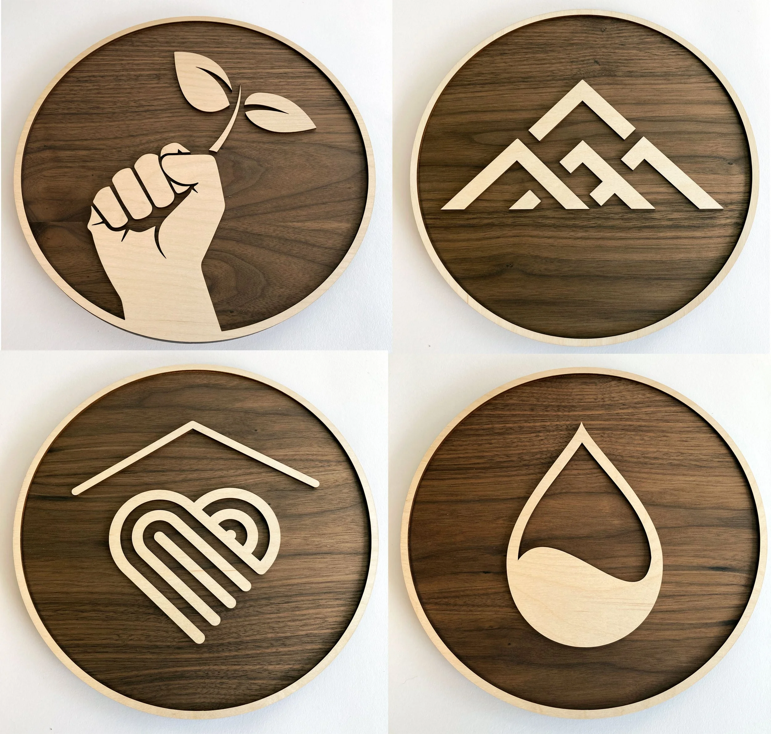 CO2 laser cut maple and walnut layered circular wooden plaques with a clenched fist holding a plant and stylized mountain peaks designs, custom laser cutting by MC Laser Labs.