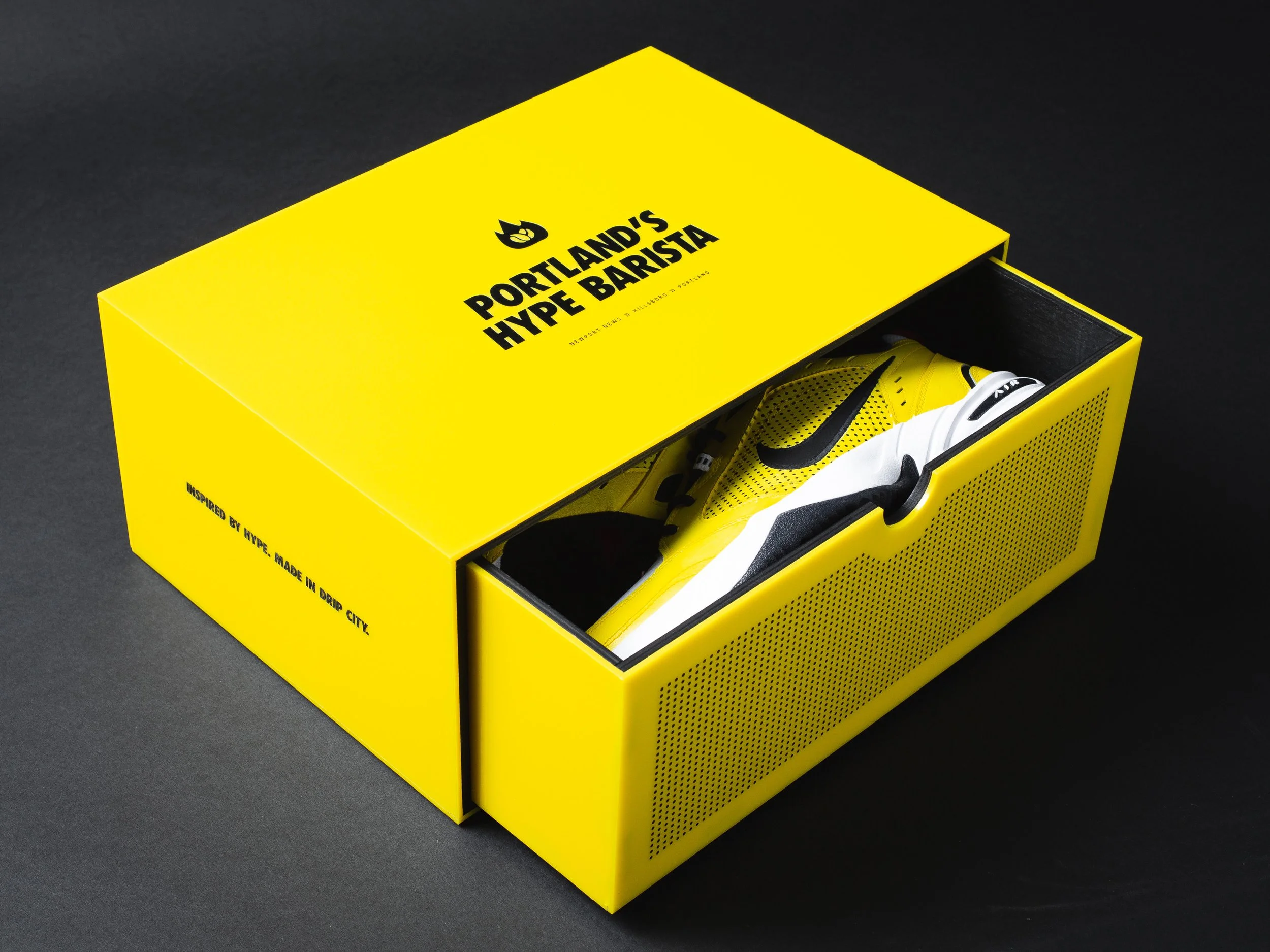 Yellow shoebox with black text reading 'Portland's Hype Barista' and partially visible yellow and black sneakers inside, on a dark surface.