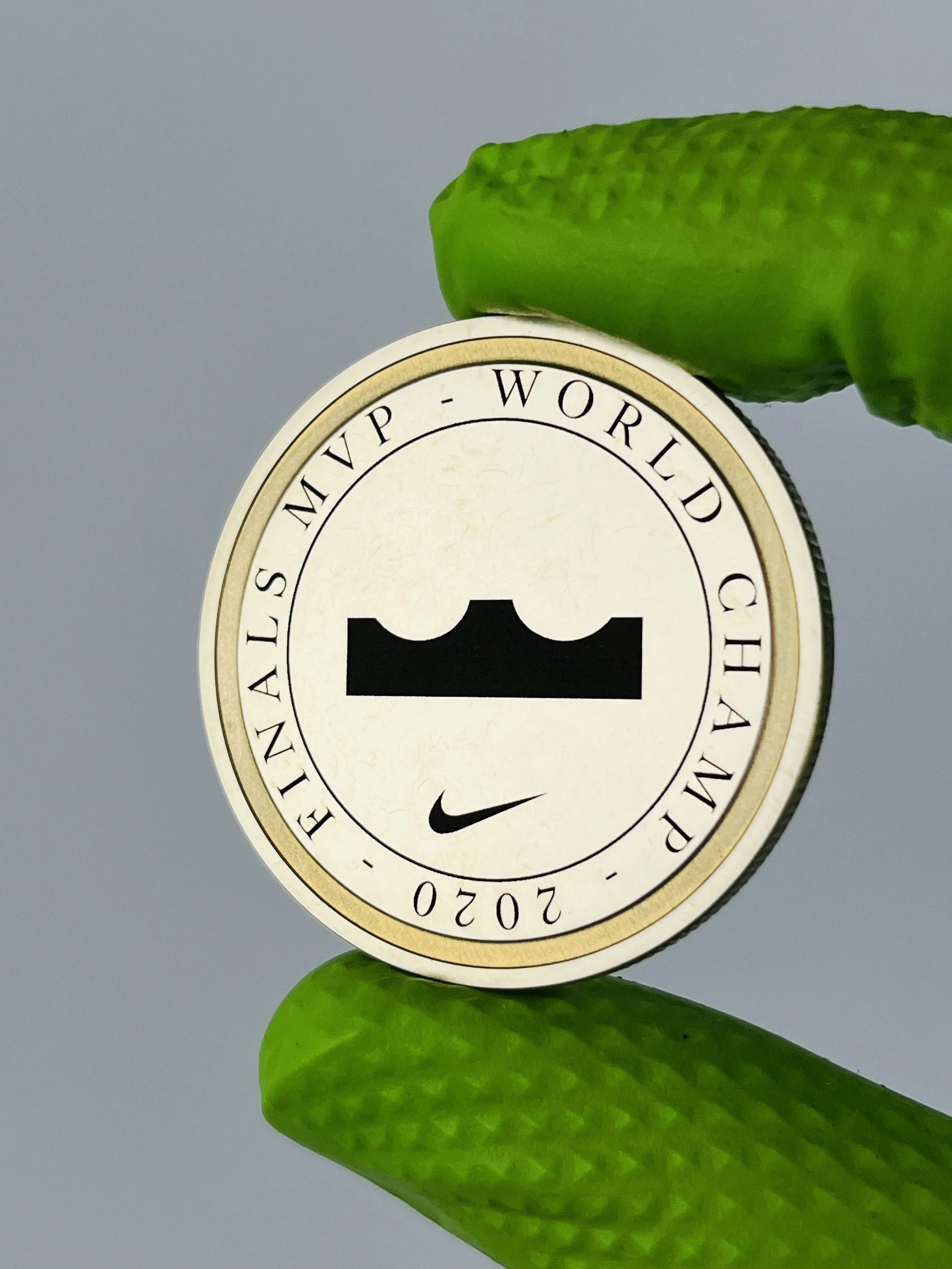 Close-up of a round sticker with the Nike logo and the year 2020, placed on a green leaf with textured surface, against a plain gray background.