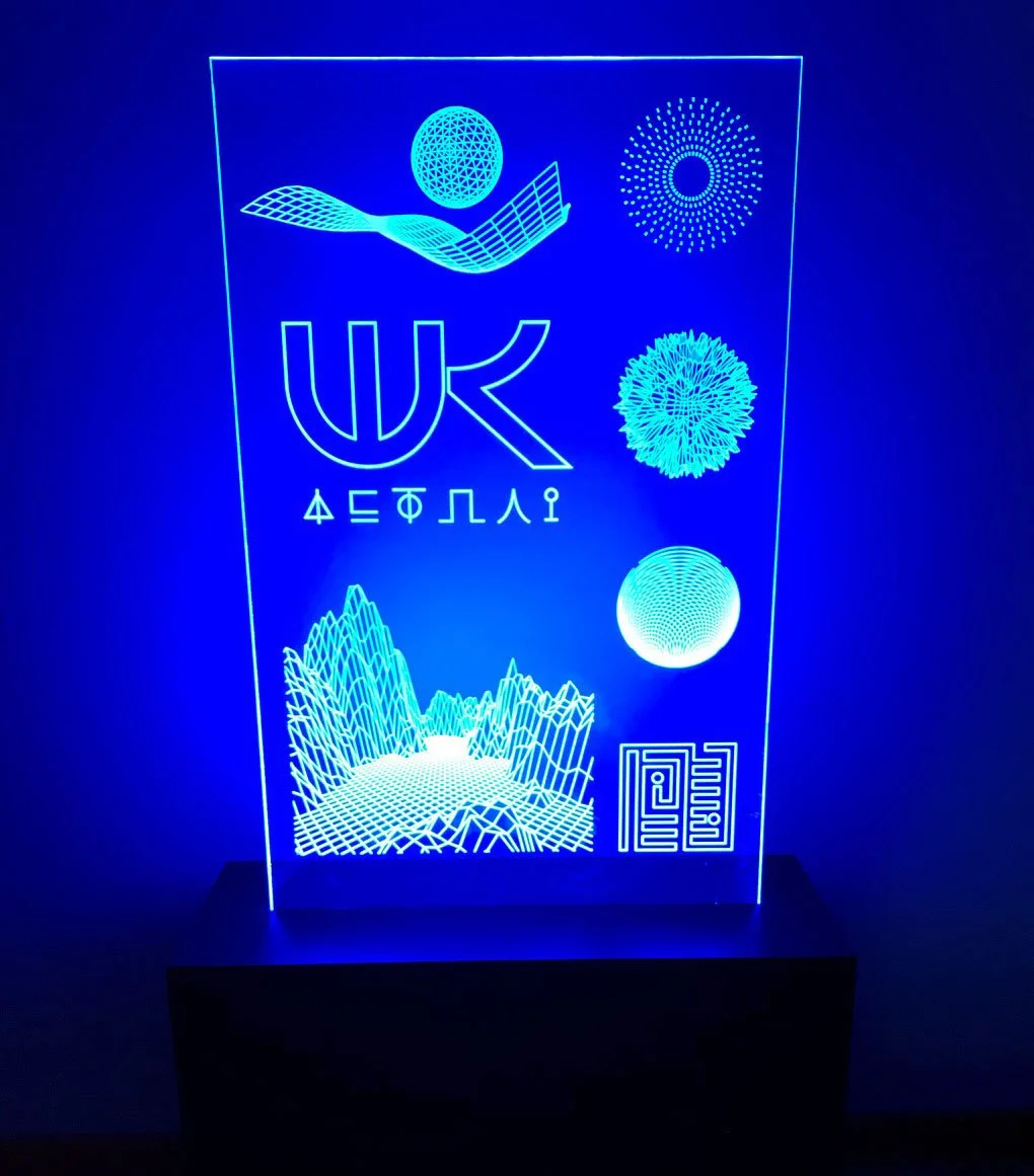 Blue glowing light-up LED acrylic sign with geometric designs, the word 'W+K', Greek text, and landscape and circular designs, custom laser cutting and fabrication by MC Laser Labs in Portland, OR.