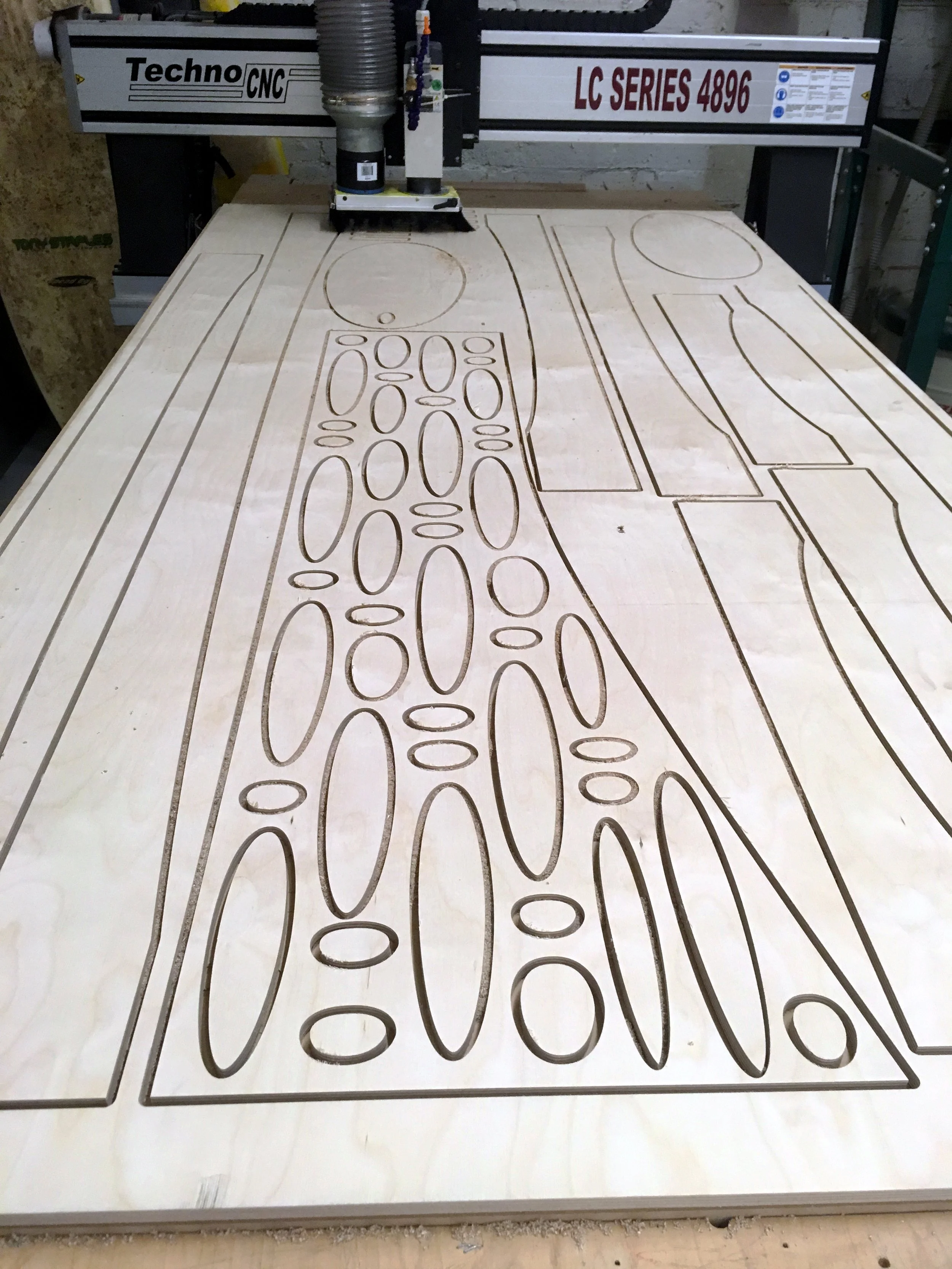 Laser cutter etching various oval and linear shapes into a piece of wood.