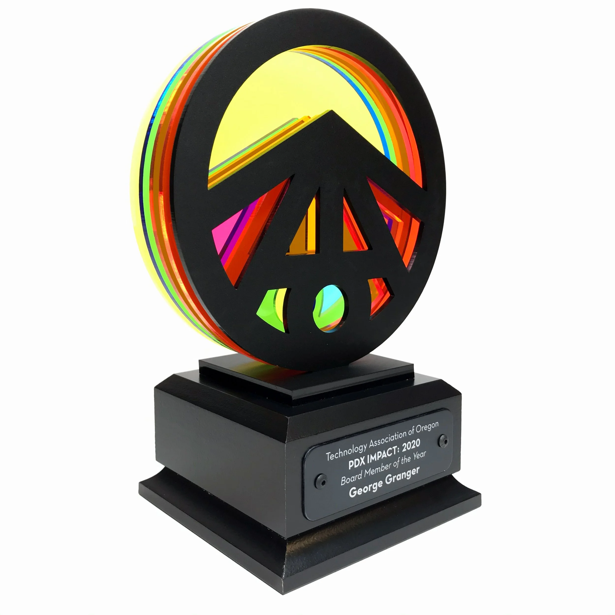 CO2 laser cut layered neon acrylic award trophy with a rainbow-colored logo, mounted on a black base with an inscription plaque, custom laser cutting and fabrication by MC Laser Labs.