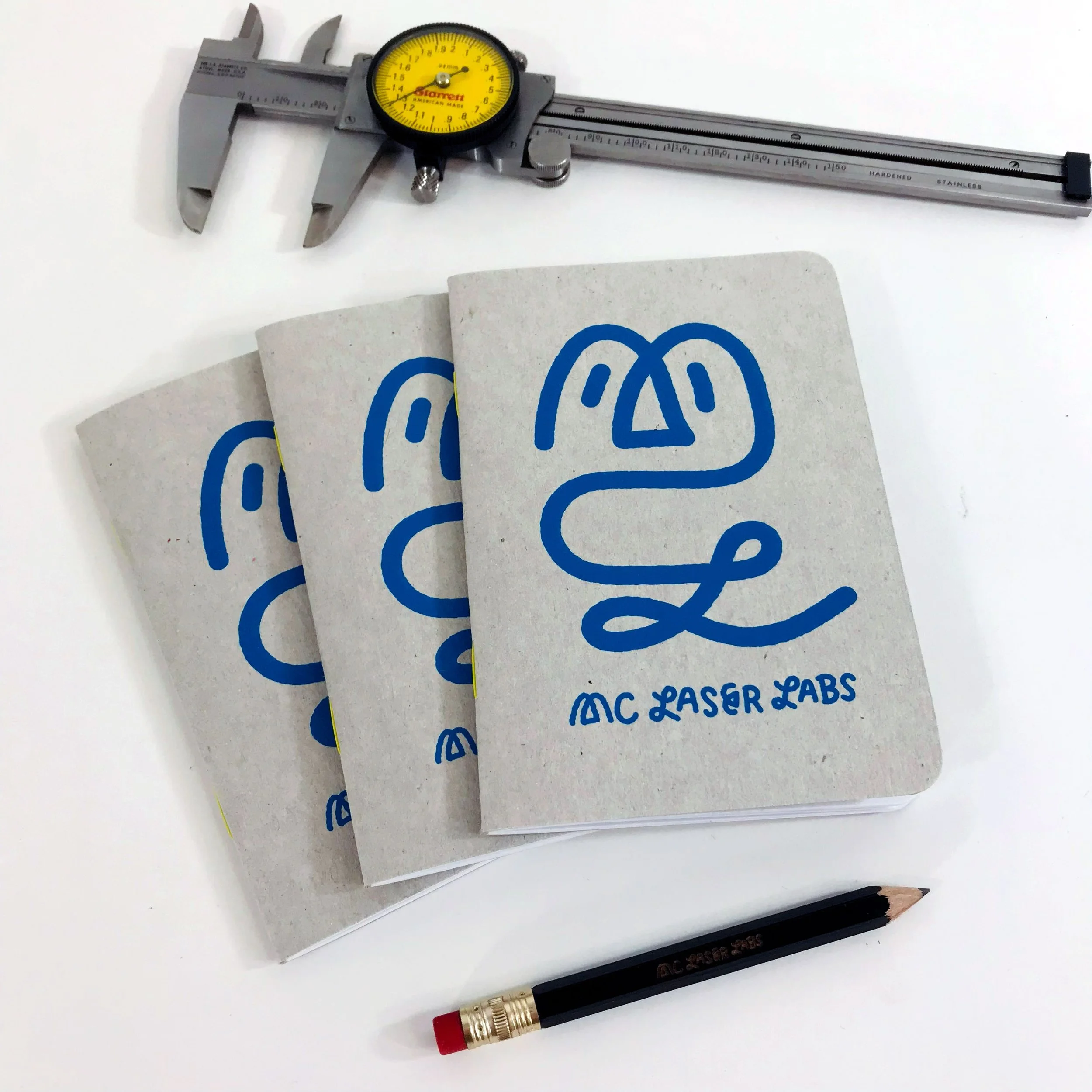 A pair of gray calipers, a black pencil with a red eraser, and a PCA Laser Labs logo card on a white surface.