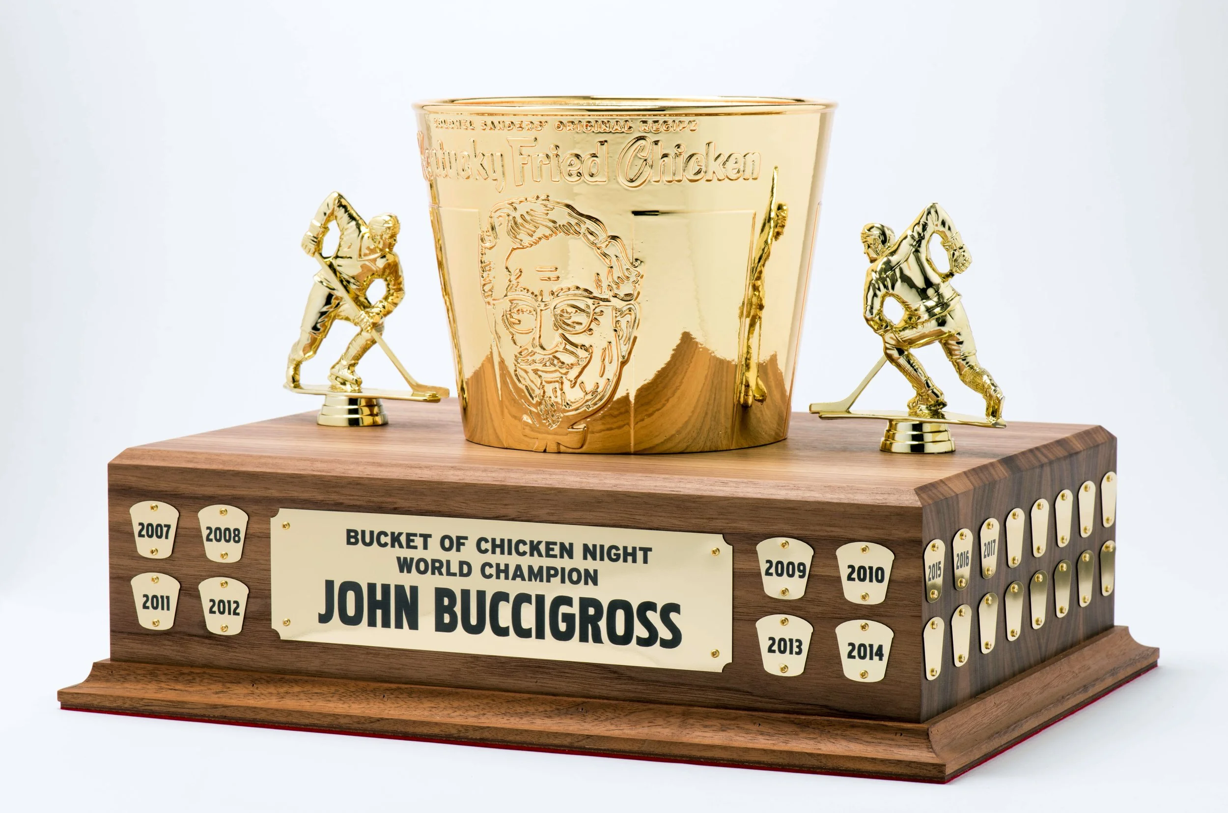 Custom-made trophy for 'Bucket of Chicken Night World Champion John Buccigross'.  Cusotm 3D Printed KFC Bucket that was gold chrome painted. CO2 laser cut and engraved golden 'Chicken Fried Chicken' trophy with a chef's face illustration, flanked by 