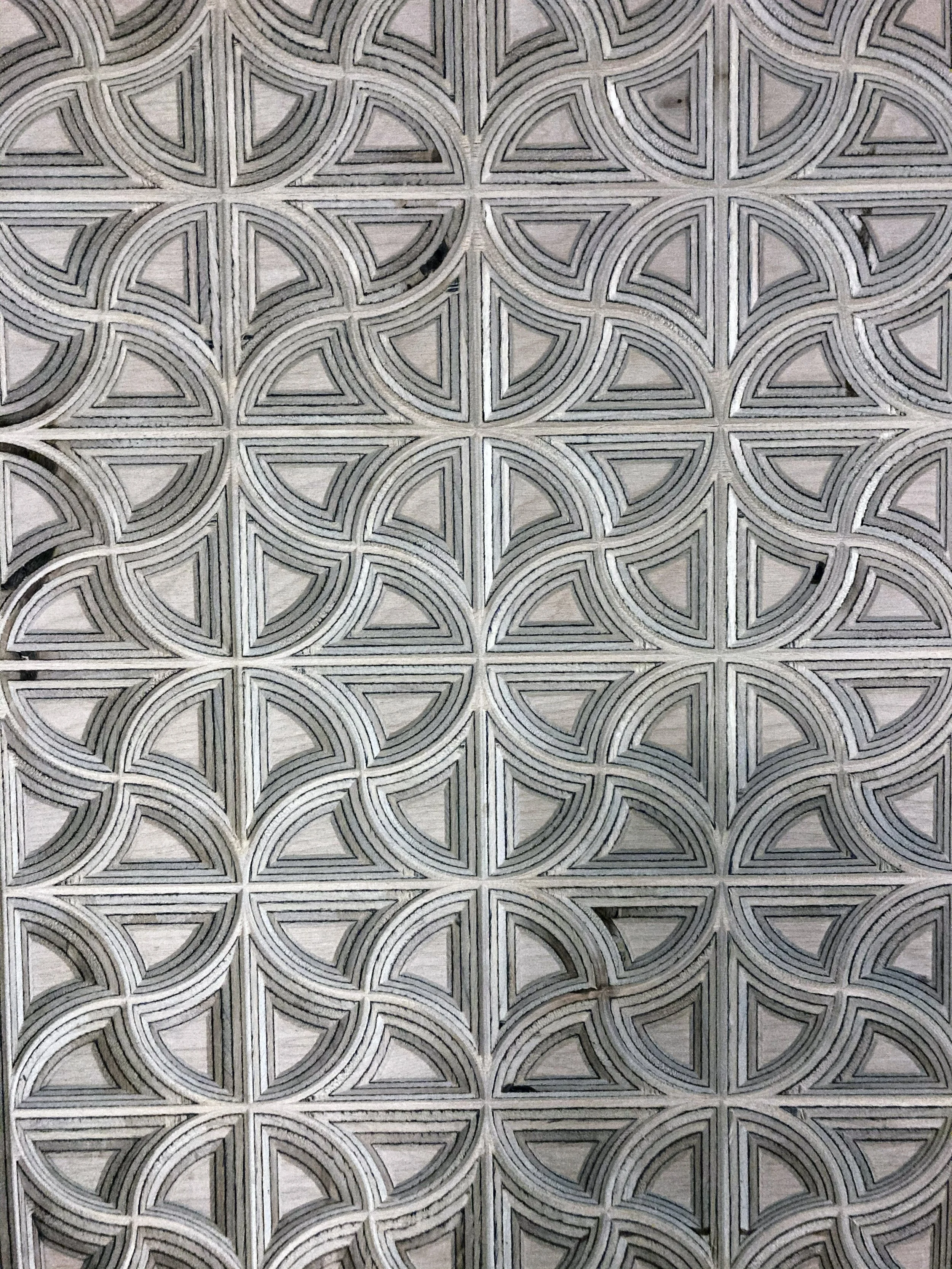 A tiled surface with repeating geometric patterns of semi-circles and triangles, primarily in shades of gray and white.