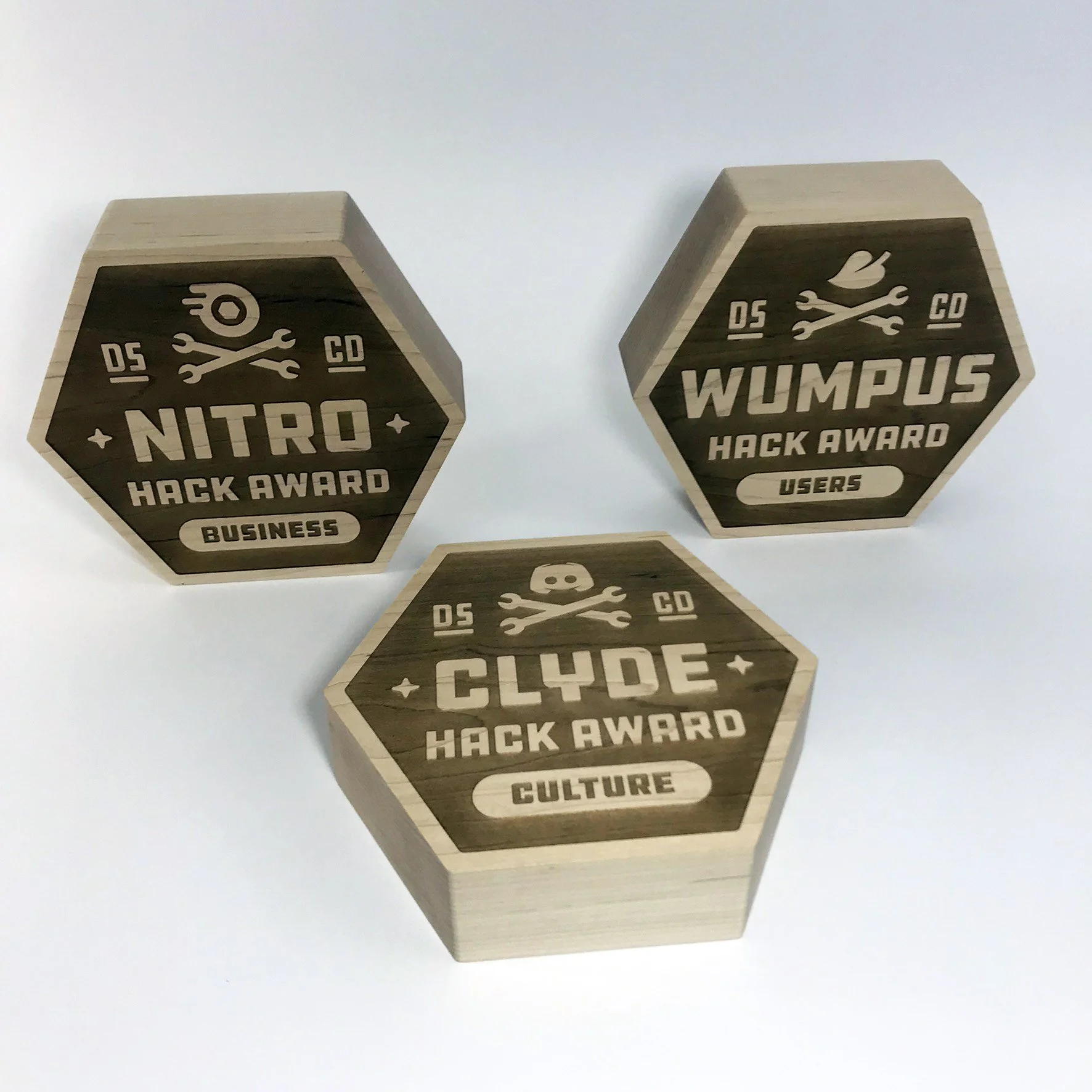 CO2 laser cut and engraved wooden hackathon award trophies labeled 'Business' and 'Users', each featuring a crossed wrench and gear symbol, custom laser cutting and engraving by MC Laser Labs.