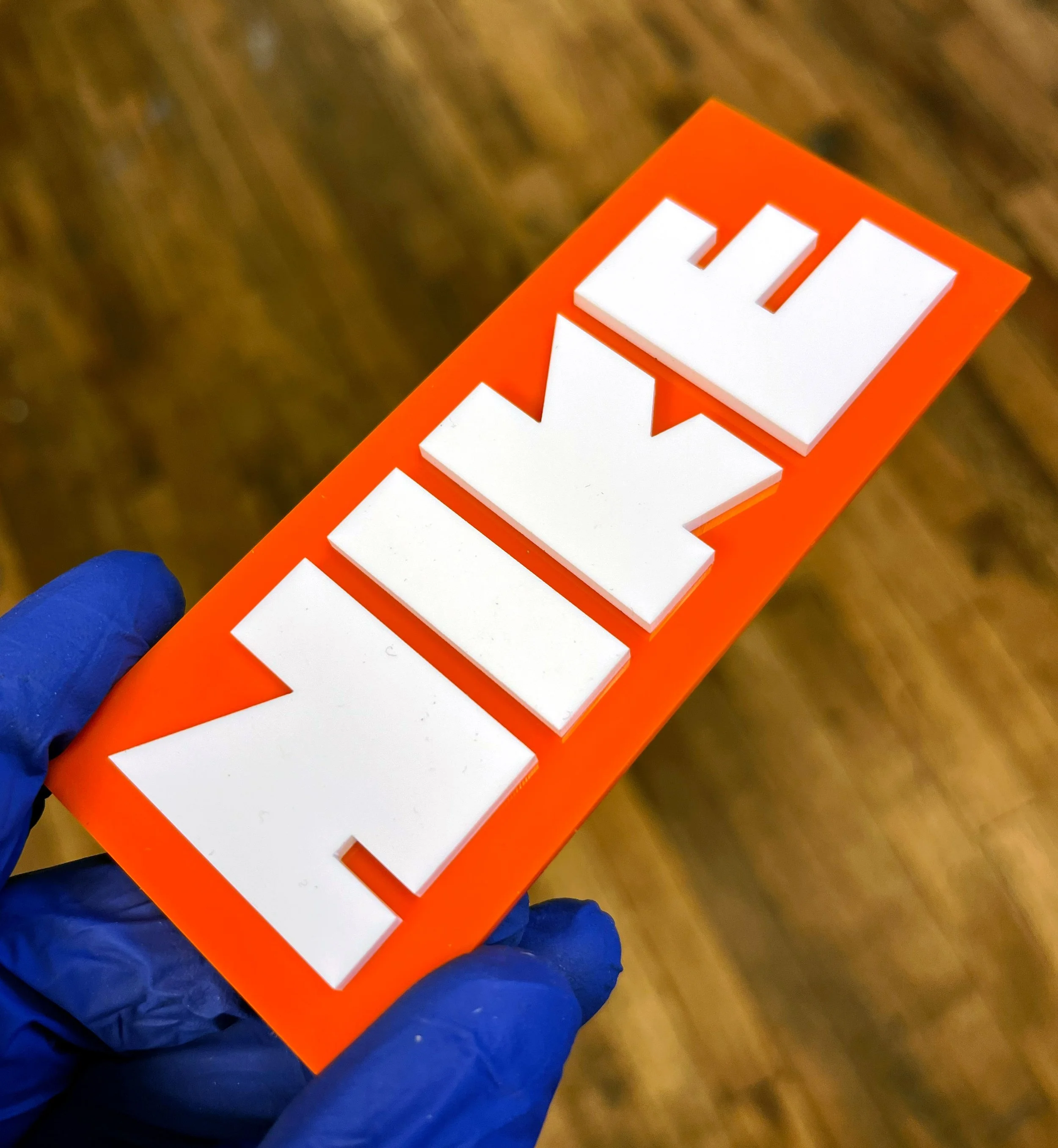 Nike-branded packaging with white wooden blocks spelling 'HELP', held in a blue-gloved hand, custom laser fabrication by MC Laser Labs.
