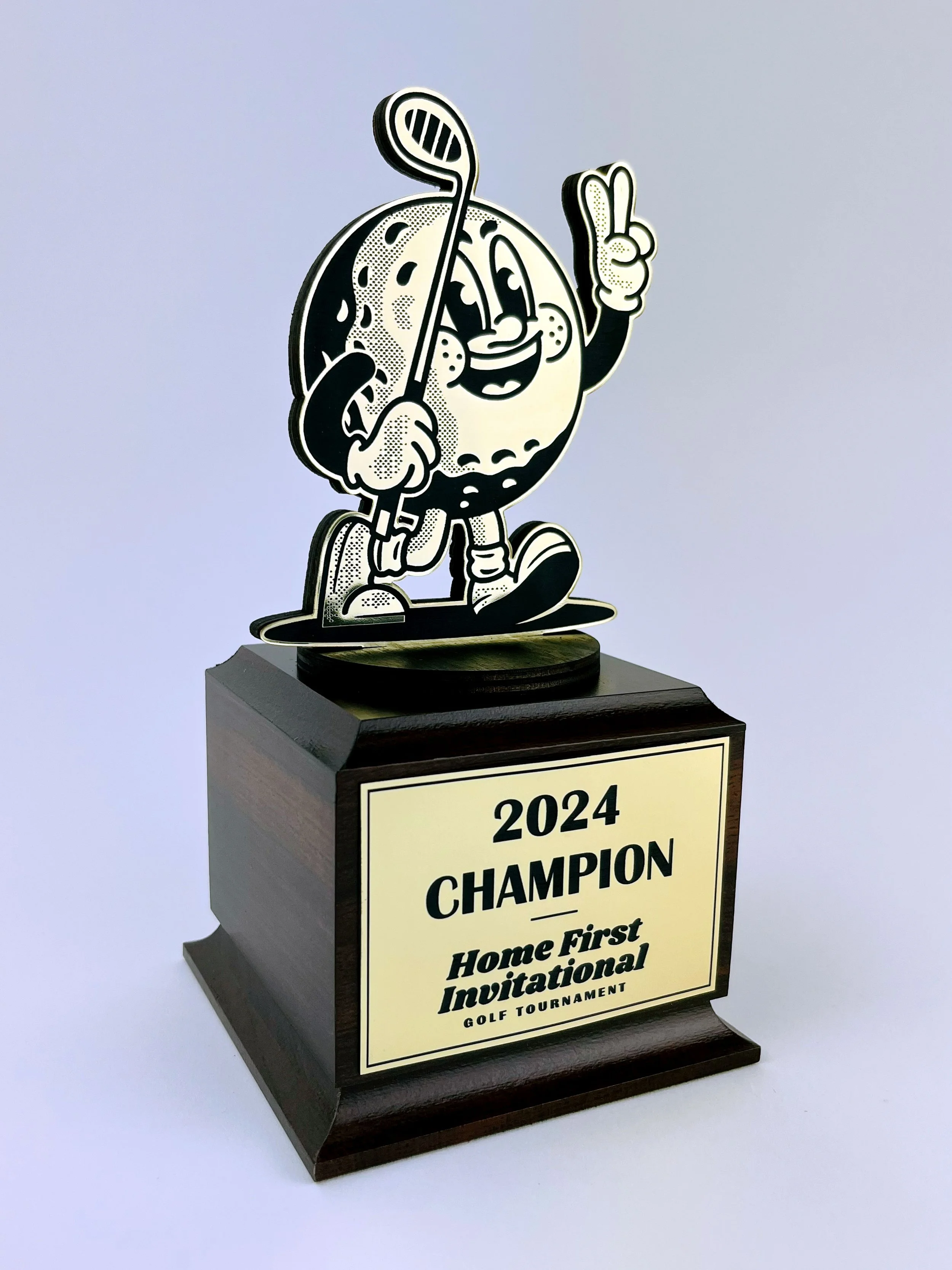 CO2 laser cut and engraved wooden trophy with a cartoon golf ball character holding a club, commemorating the 2024 Home First Invitational Golf Tournament, custom laser cutting and engraving by MC Laser Labs.