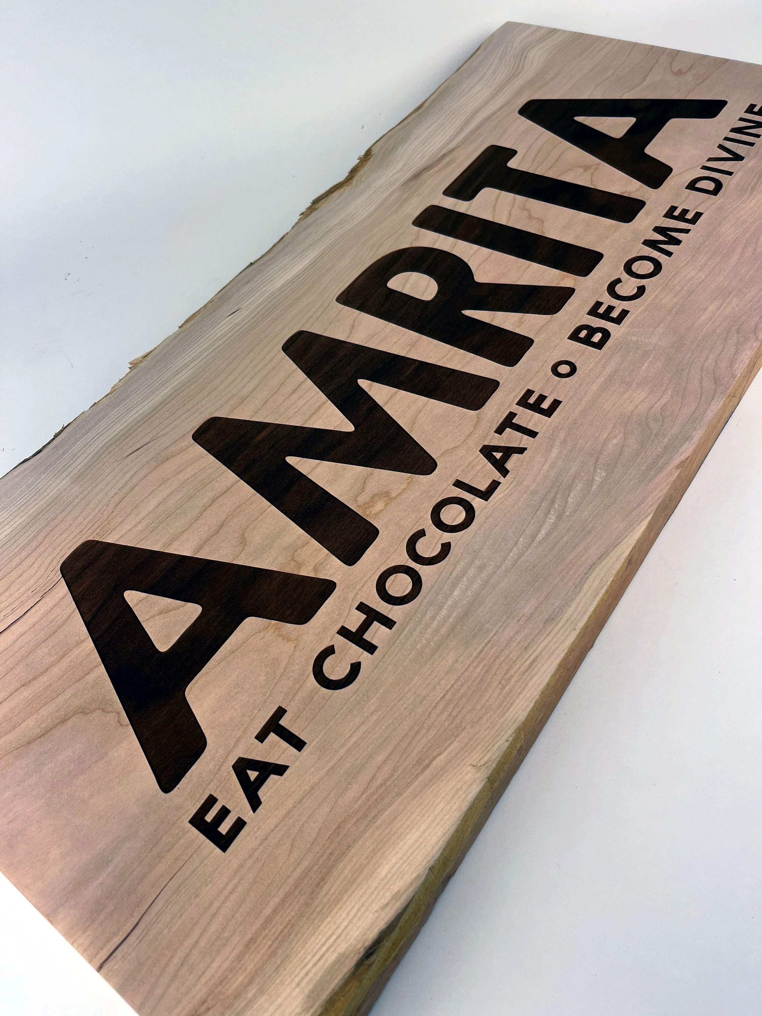 CO2 laser engraved wooden sign reading 'AMRITA FAVIA' with the phrase 'TO BLEACH ONE DIVINE', custom laser engraving by MC Laser Labs.