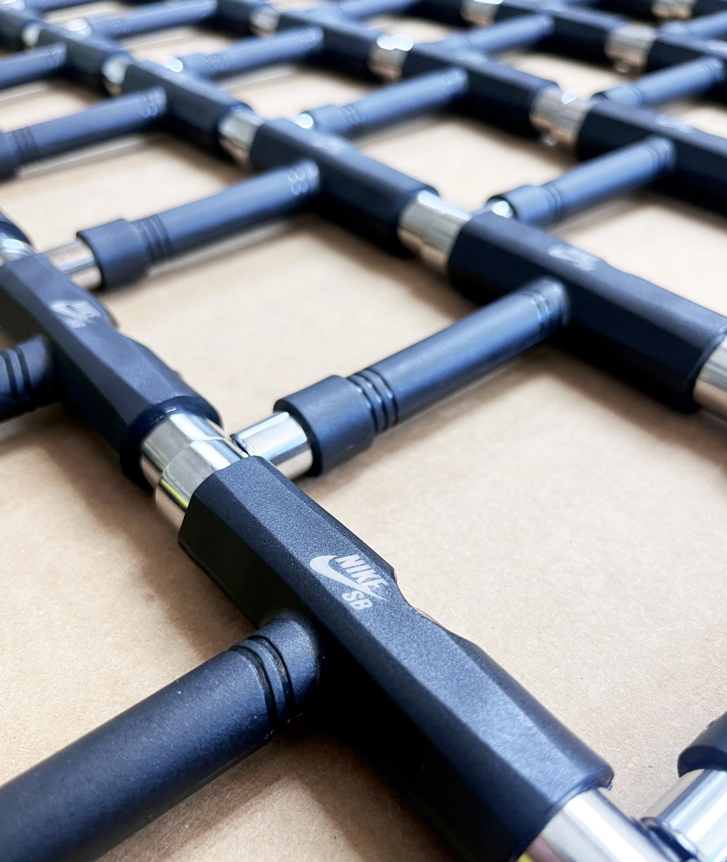 Close-up of black Nike SB skateboard trucks with silver axles on a wooden surface.