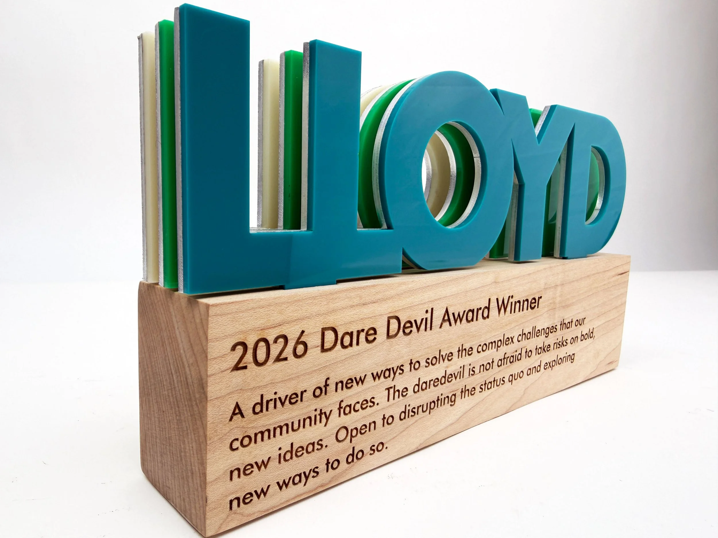 CO2 laser cut colorful acrylic letters spelling 'LLOYD' on a wooden base with engraved text, custom laser cutting and engraving by MC Laser Labs. Custom fabrication in Portland Oregon