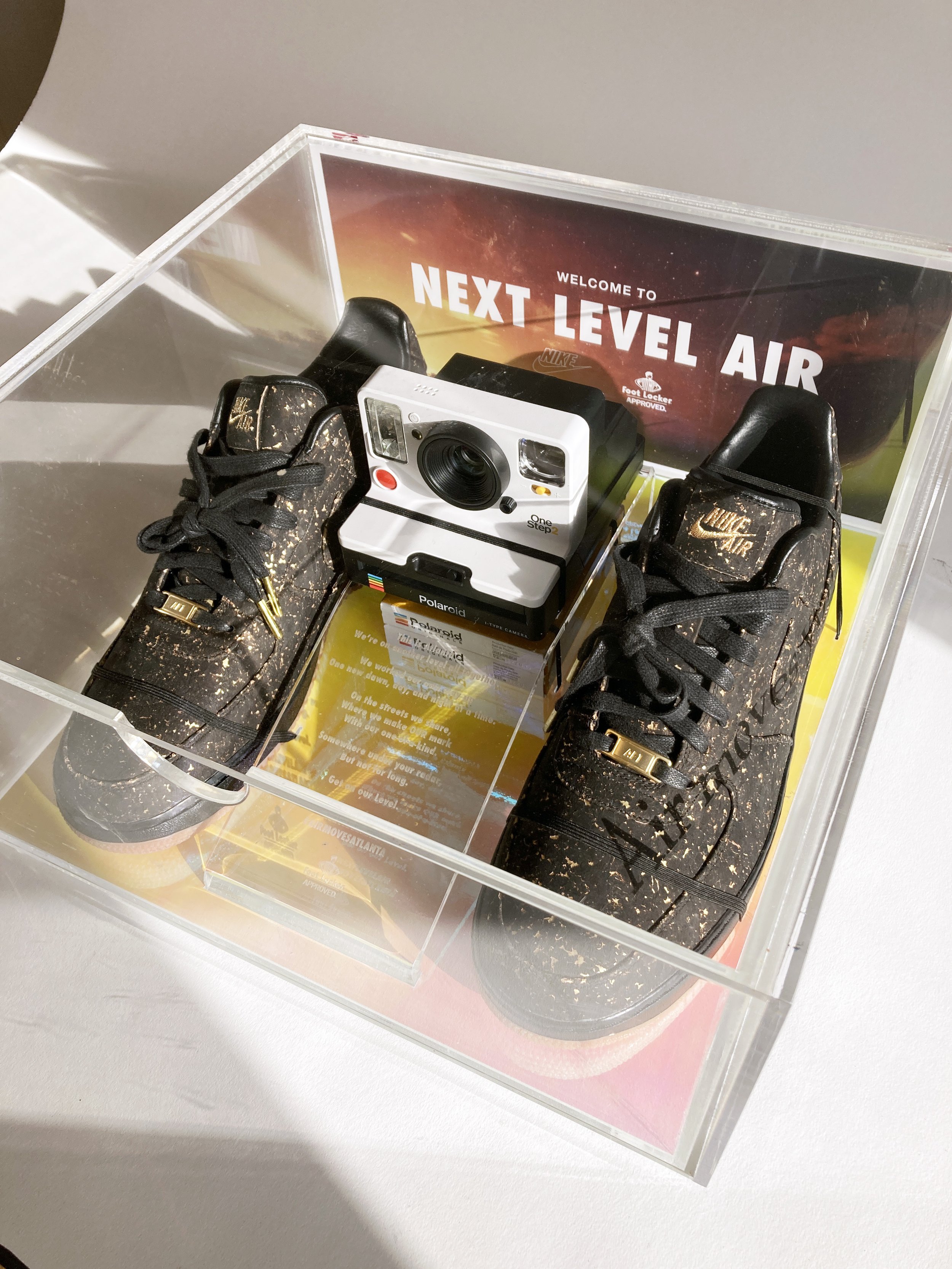 Nike 'Next Level Air' acrylic seeding kit display case with black and gold splatter Nike Air sneakers and a Polaroid One Step 2 camera, custom fabrication by MC Laser Labs.