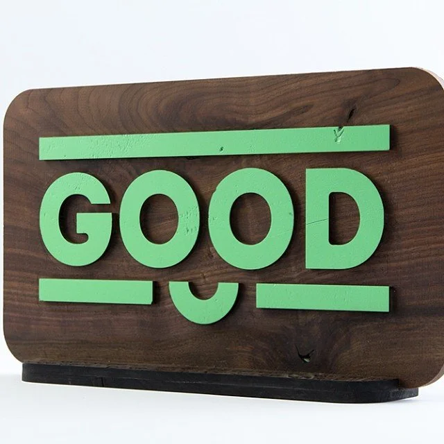 Decorative wooden sign with the word 'GOOD' in large green letters, featuring a smiley face motif underneath.