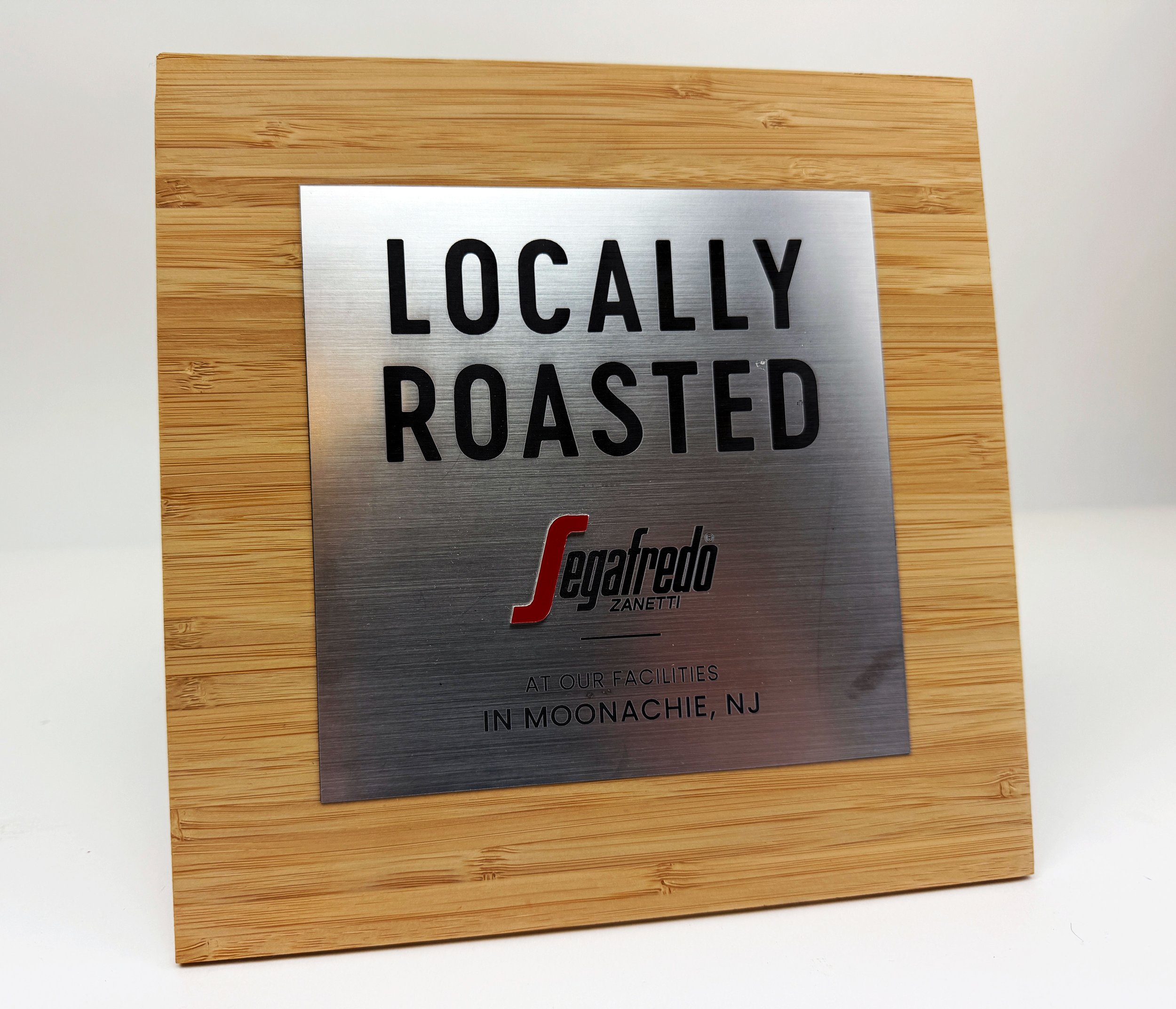 CO2 laser cut and engraved metal sign reading 'Locally Roasted', mounted on a wooden surface, custom laser cutting and engraving by MC Laser Labs.