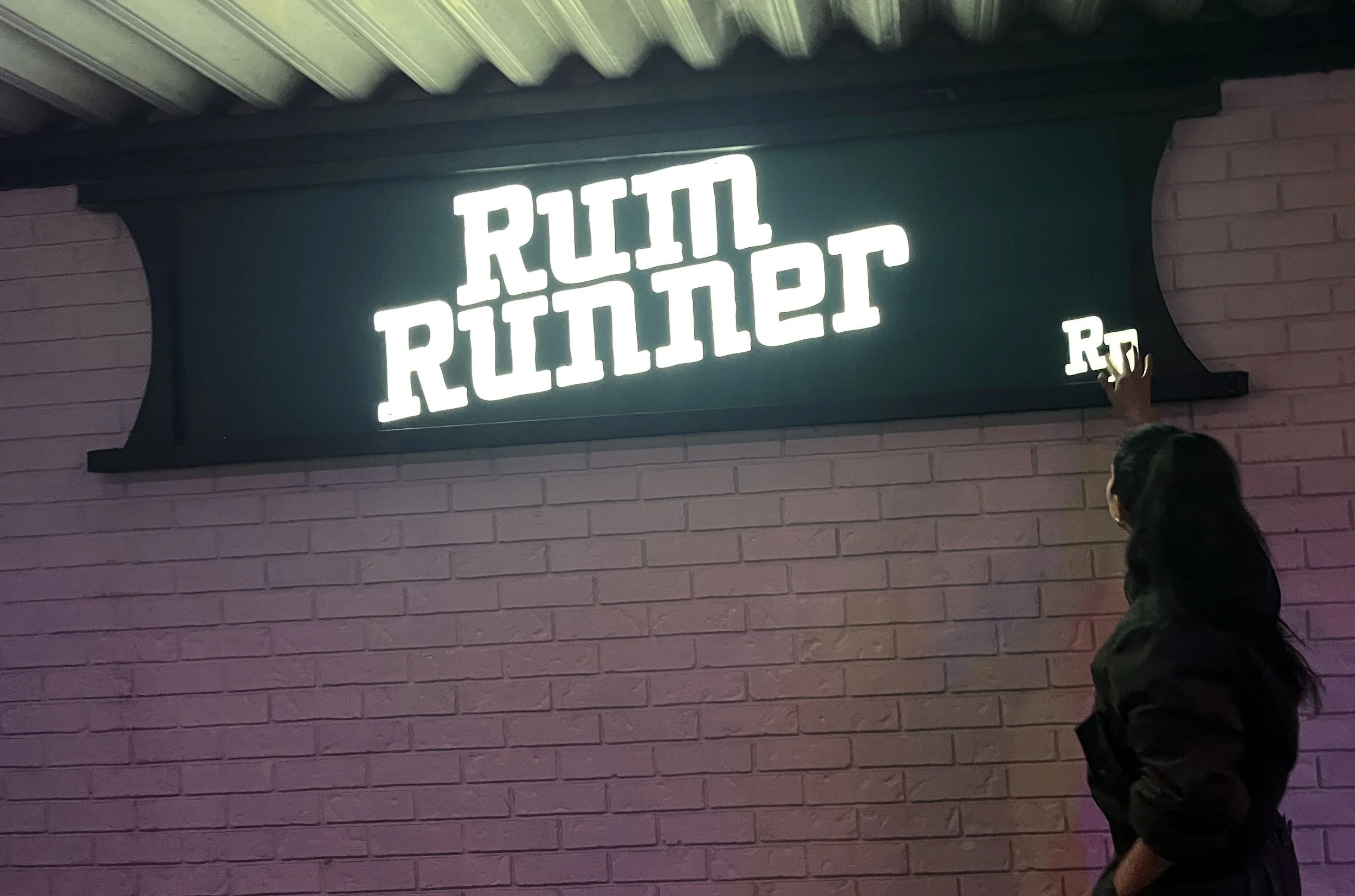 Backlit sign reading 'Rail Ruiter' on a pink brick wall with a person in dark clothing touching the sign.