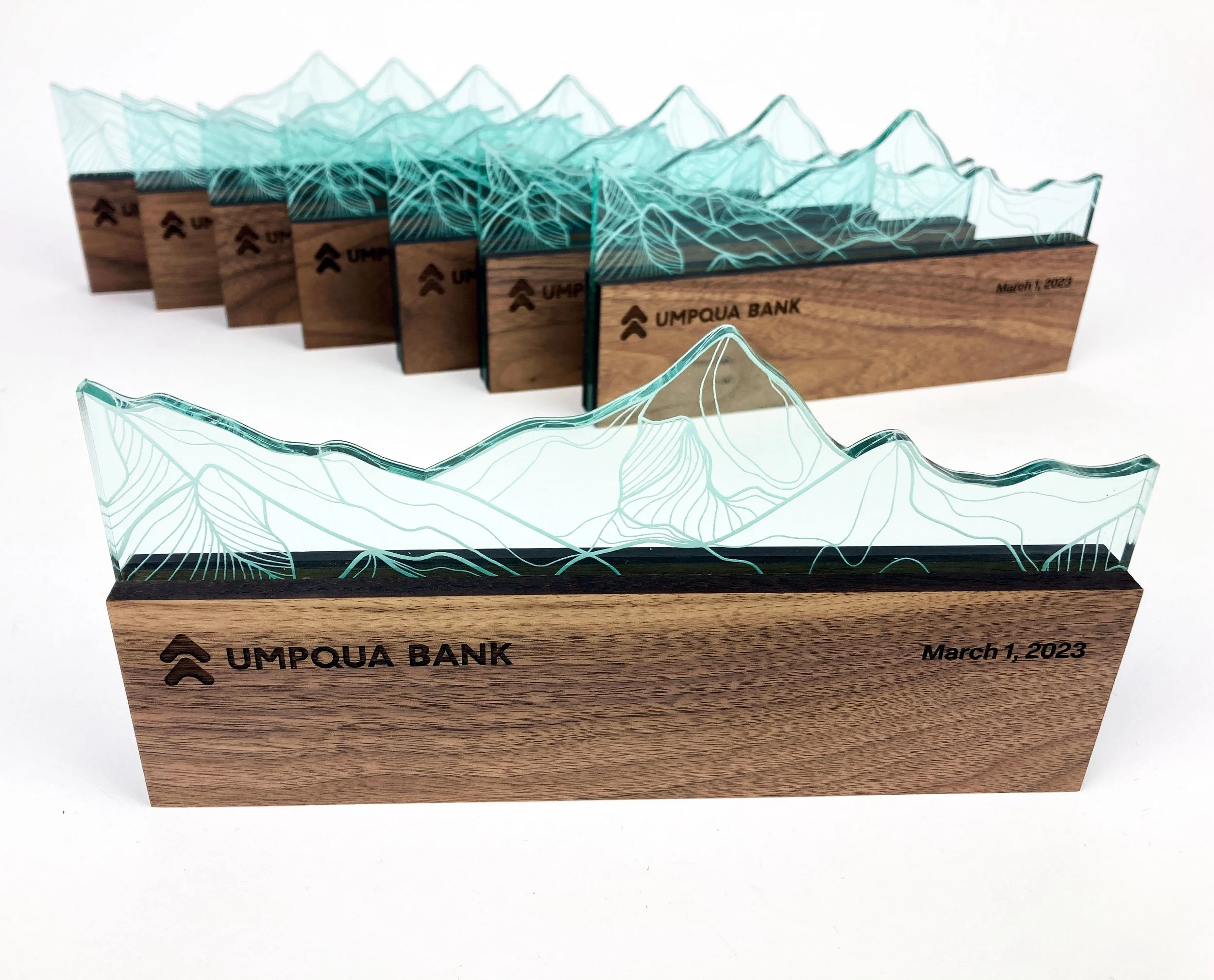 CO2 laser cut and engraved wooden and glass award plaque with topographical mountain design, engraved 'UMPQUA BANK' and dated March 1, 2023, custom laser cutting and engraving by MC Laser Labs.