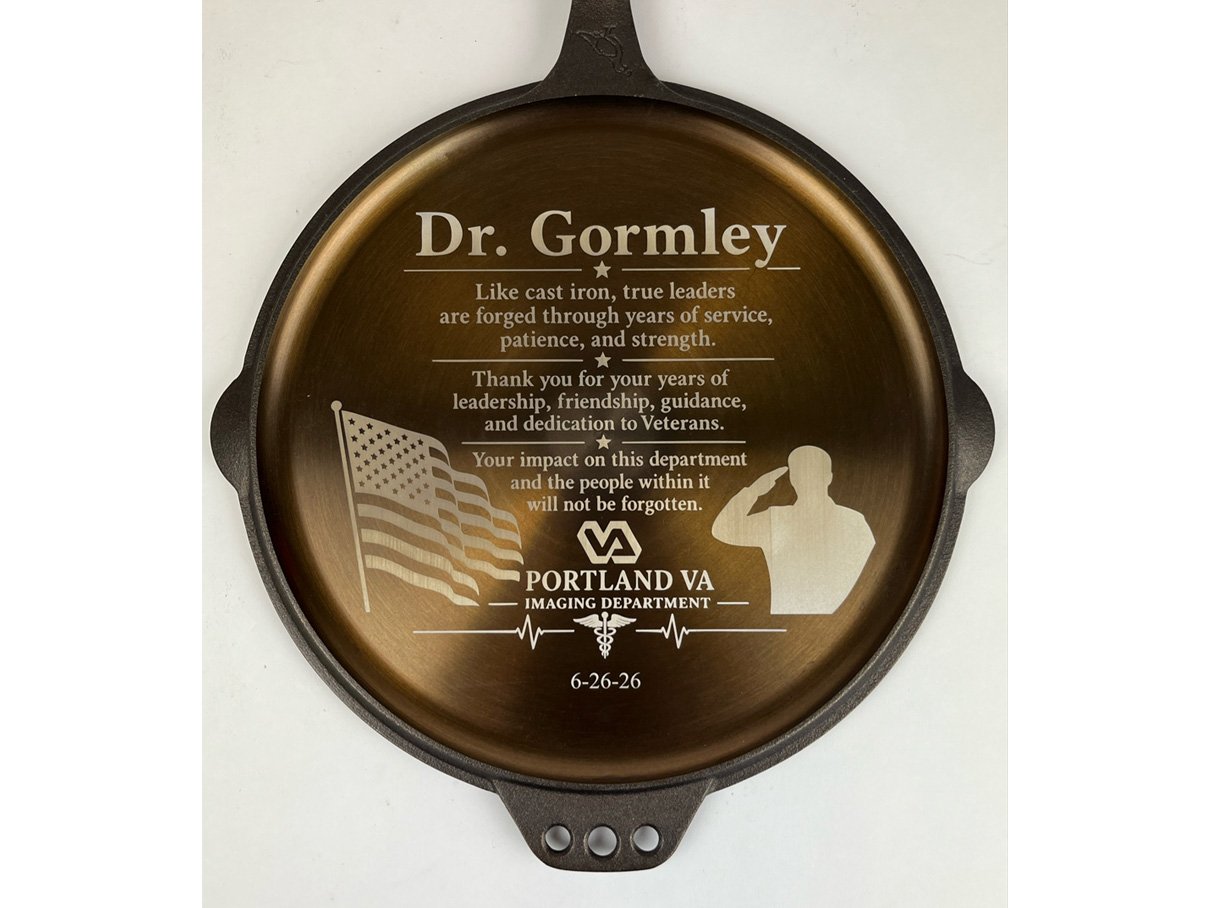 Fiber laser marked commemorative plaque on a Smithey cast iron skillet, dedicated to Dr. Gormley honoring veterans and their service from the Portland VA Imaging Department, featuring a waving American flag and saluting soldier silhouette, custom met