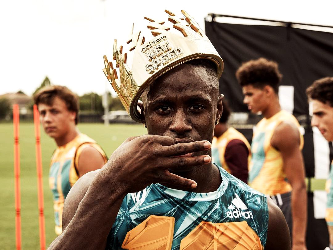 A male athlete wearing a gold adidas crown and a sports jersey, with other athletes on a sports field in the background. Custom 3D-printed crown and gold chrome-painted by MC Laser Labs custom fabrication in Portland Oregon