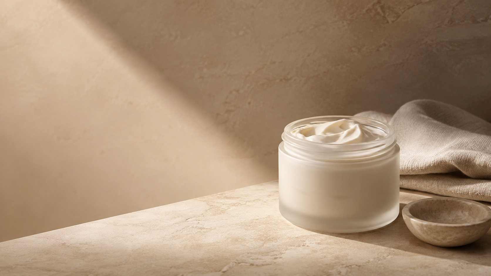 Open jar of whipped body butter on a warm beige stone surface.