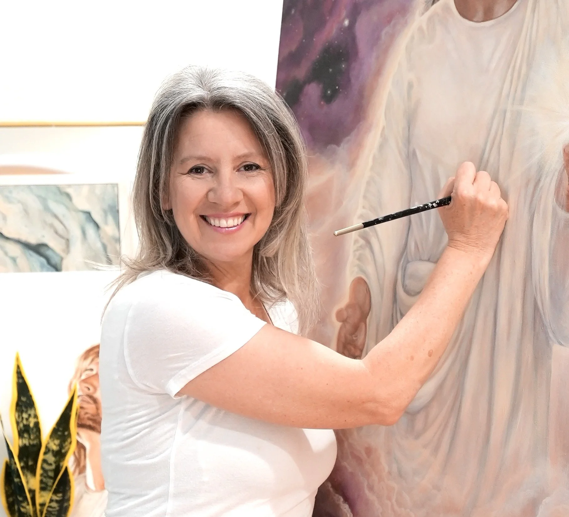 A woman with gray hair smiling while painting on a large canvas, with a galaxy-themed background.