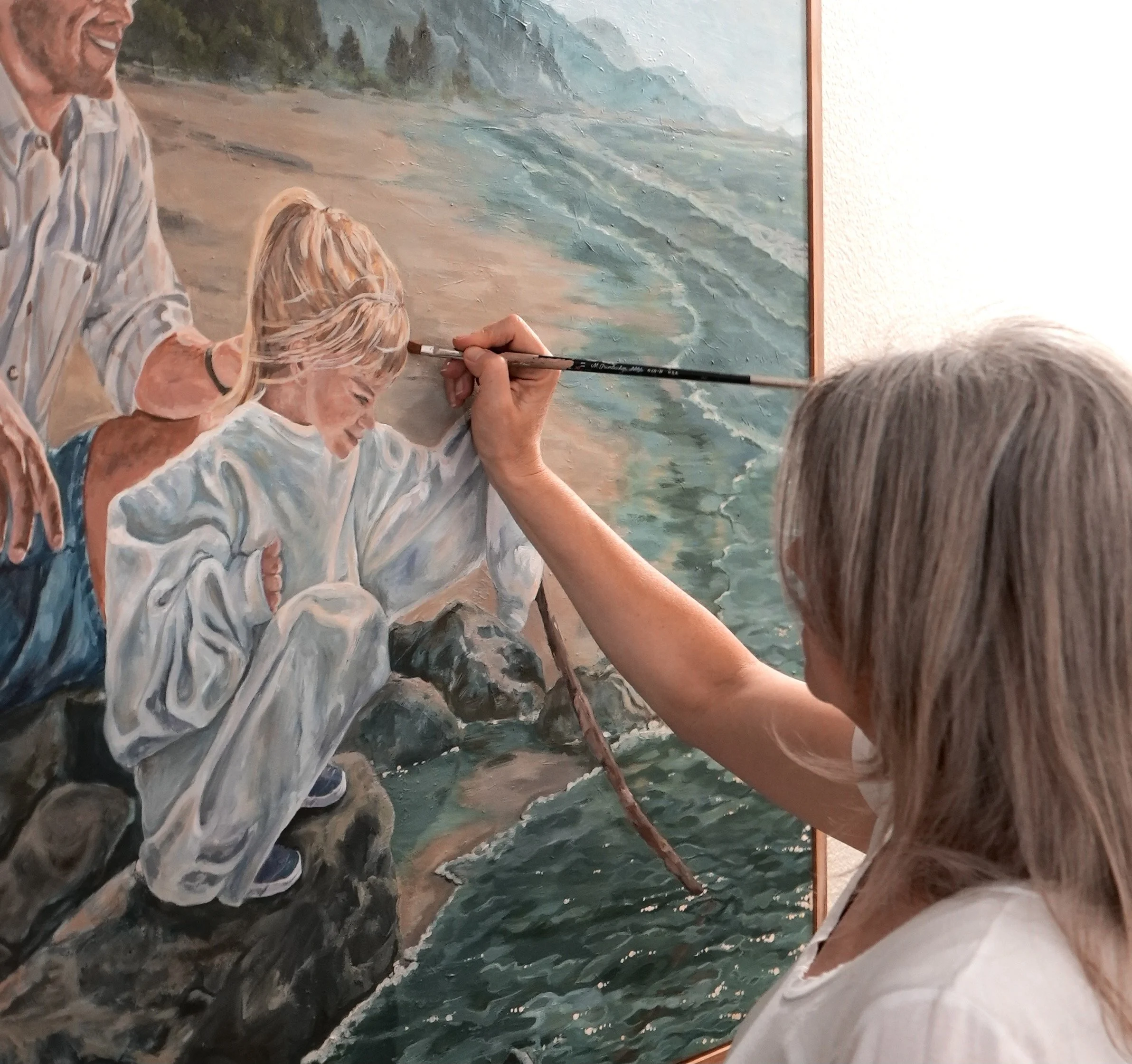 Close-up of a artist painting a detailed portrait of a father and daughter at the seashore.