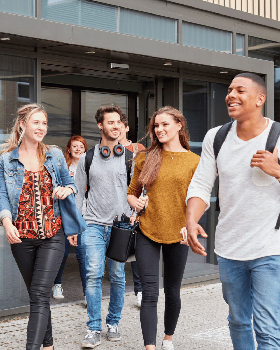 Groupe de jeunes adultes souriants sortant d'un bâtiment moderne.