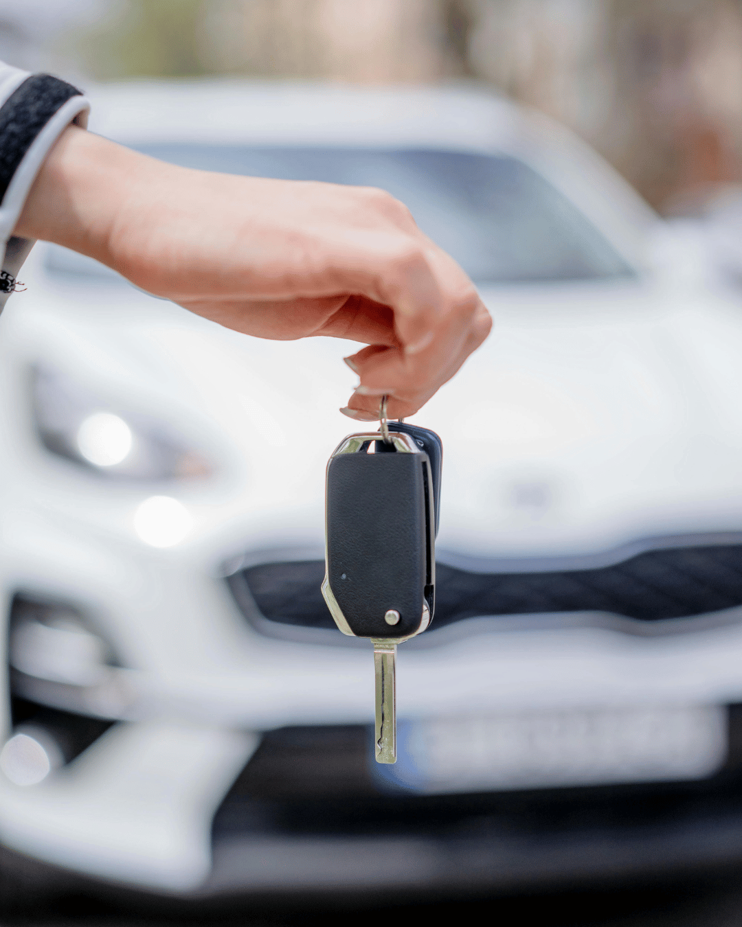 Une main tient des clés de voiture devant une voiture blanche en arrière-plan.