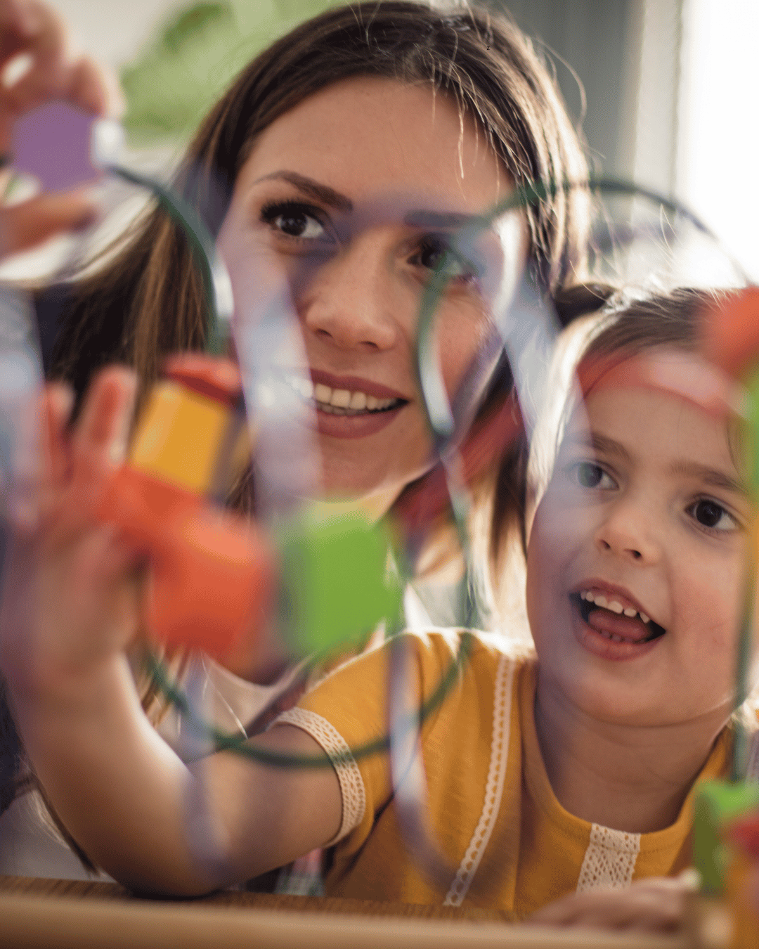 Une femme et une jeune fille regardant à travers un objet coloré, probablement un hobby ou une activité artistique, avec une expression de fascination.
