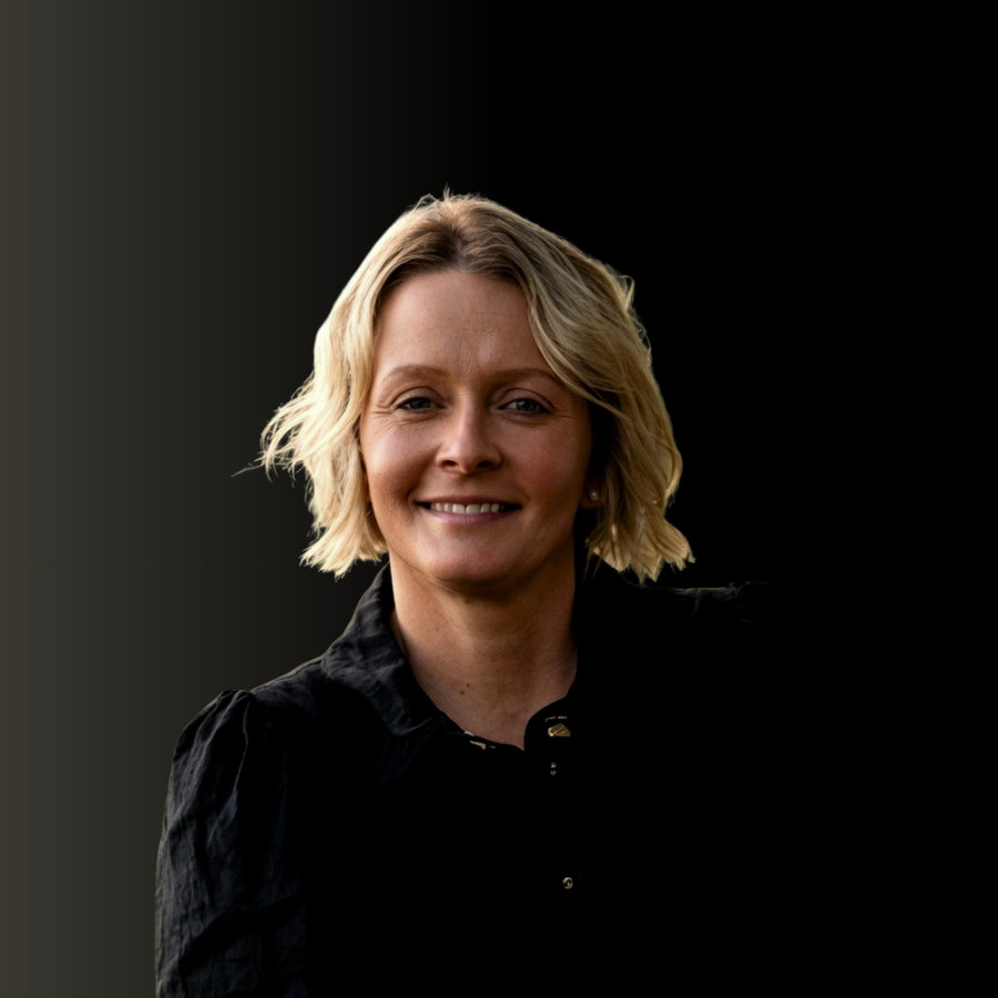 Portrait of a smiling blonde woman in a black shirt against a black background.