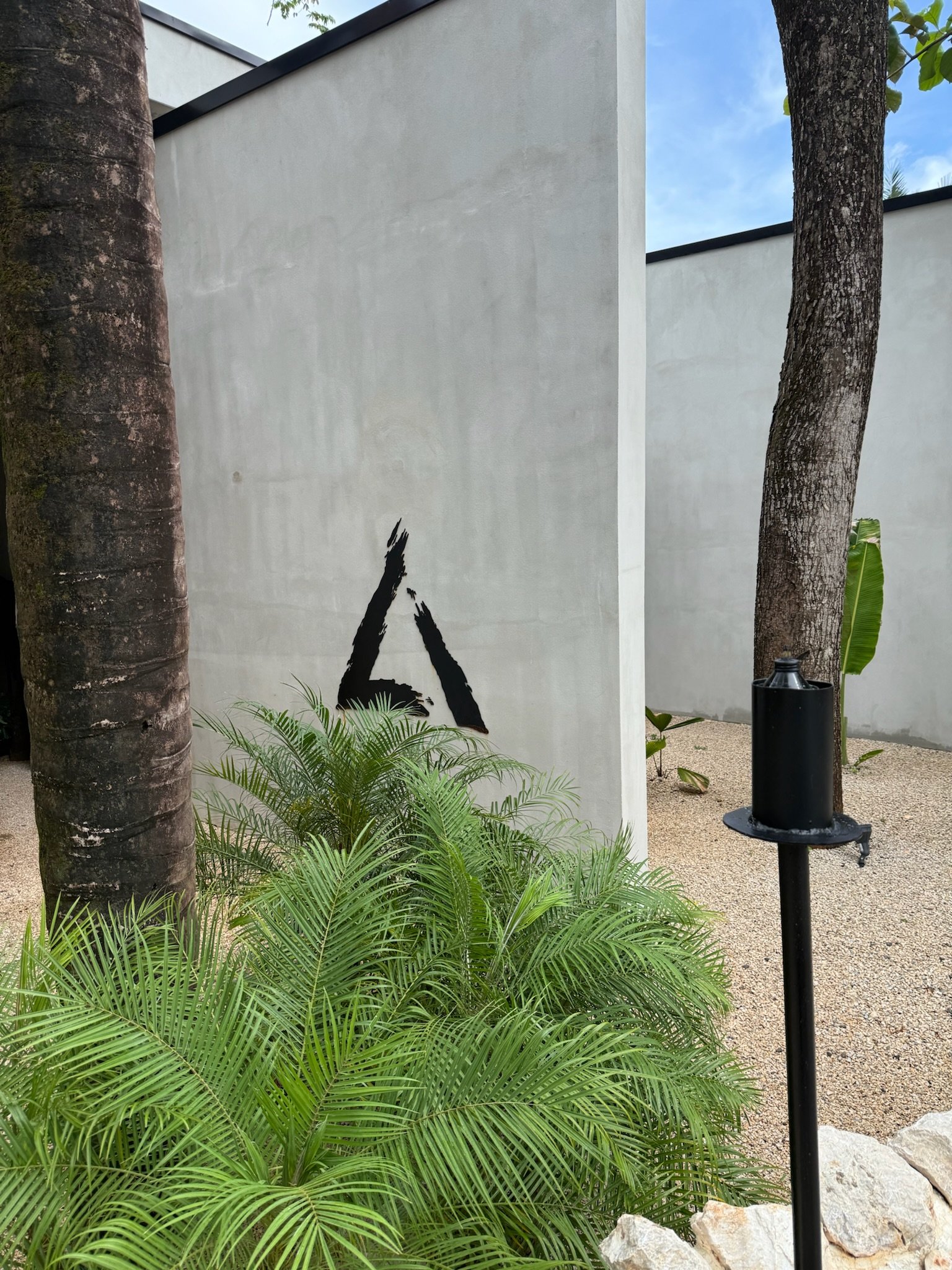 The front entrance of the Esh Hotel & Spa featuring brutalist cement architecture and palm trees